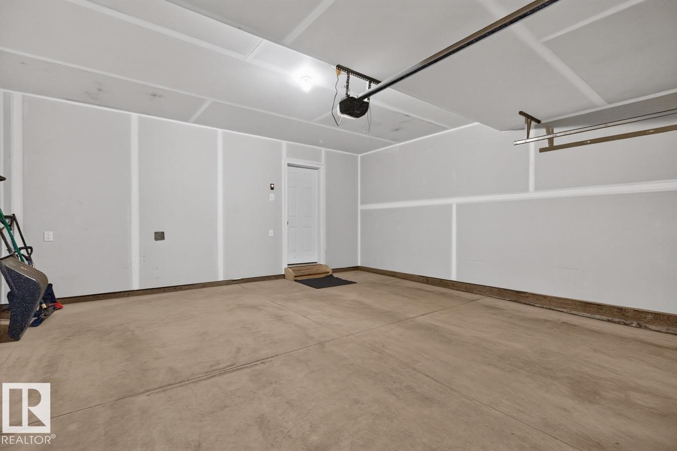 Spacious garage featuring a concrete floor, painted walls, overhead lighting, an automatic garage door opener, and a built-in storage rack - 1022 Hearthstone Boulevard, Sherwood Park, AB