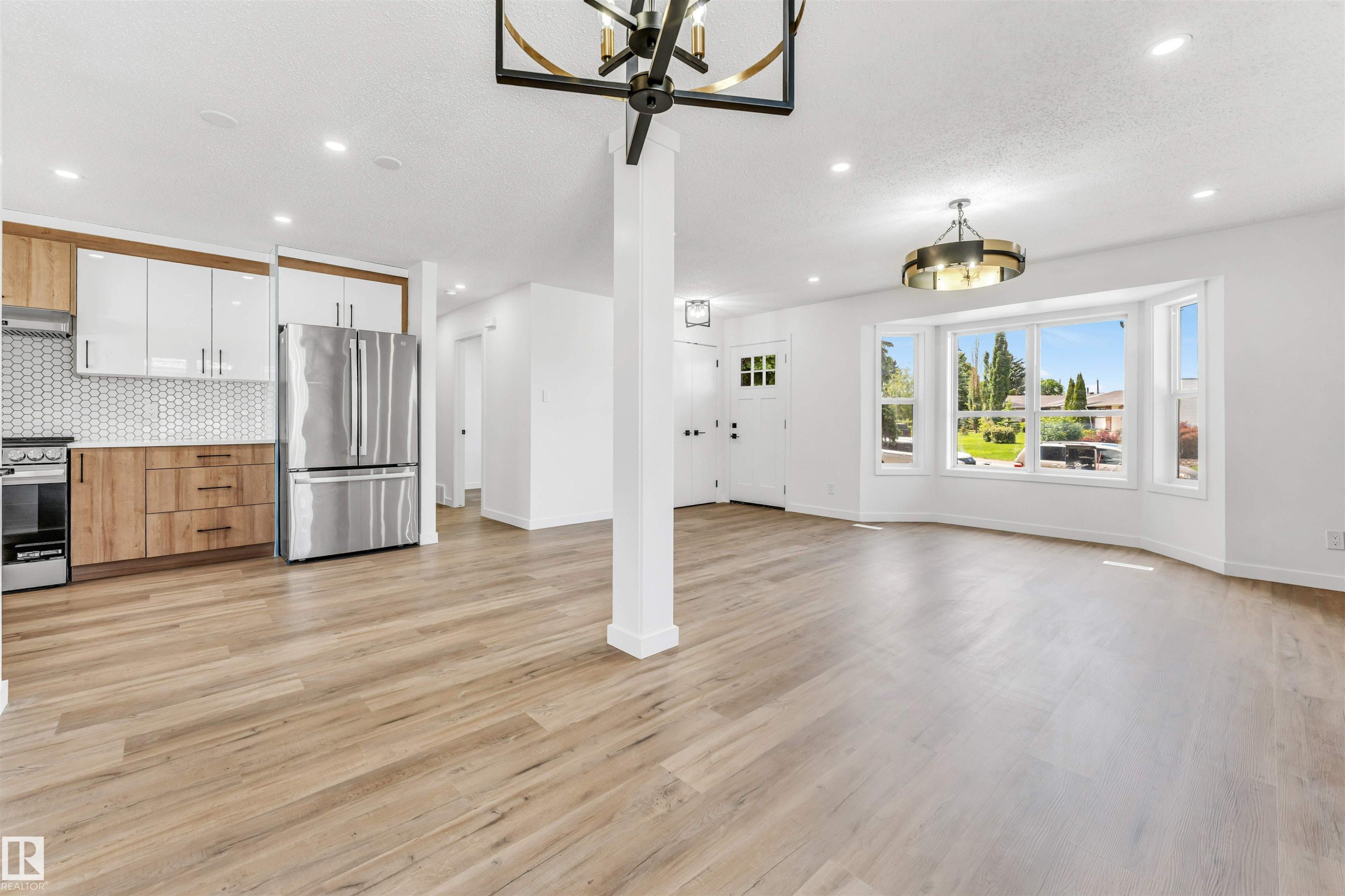 Open-concept living space featuring wood-finish flooring, a contemporary kitchen with two-tone cabinetry and geometric tile backsplash, and a prominent bay window - 6404 88 Avenue, Edmonton, AB