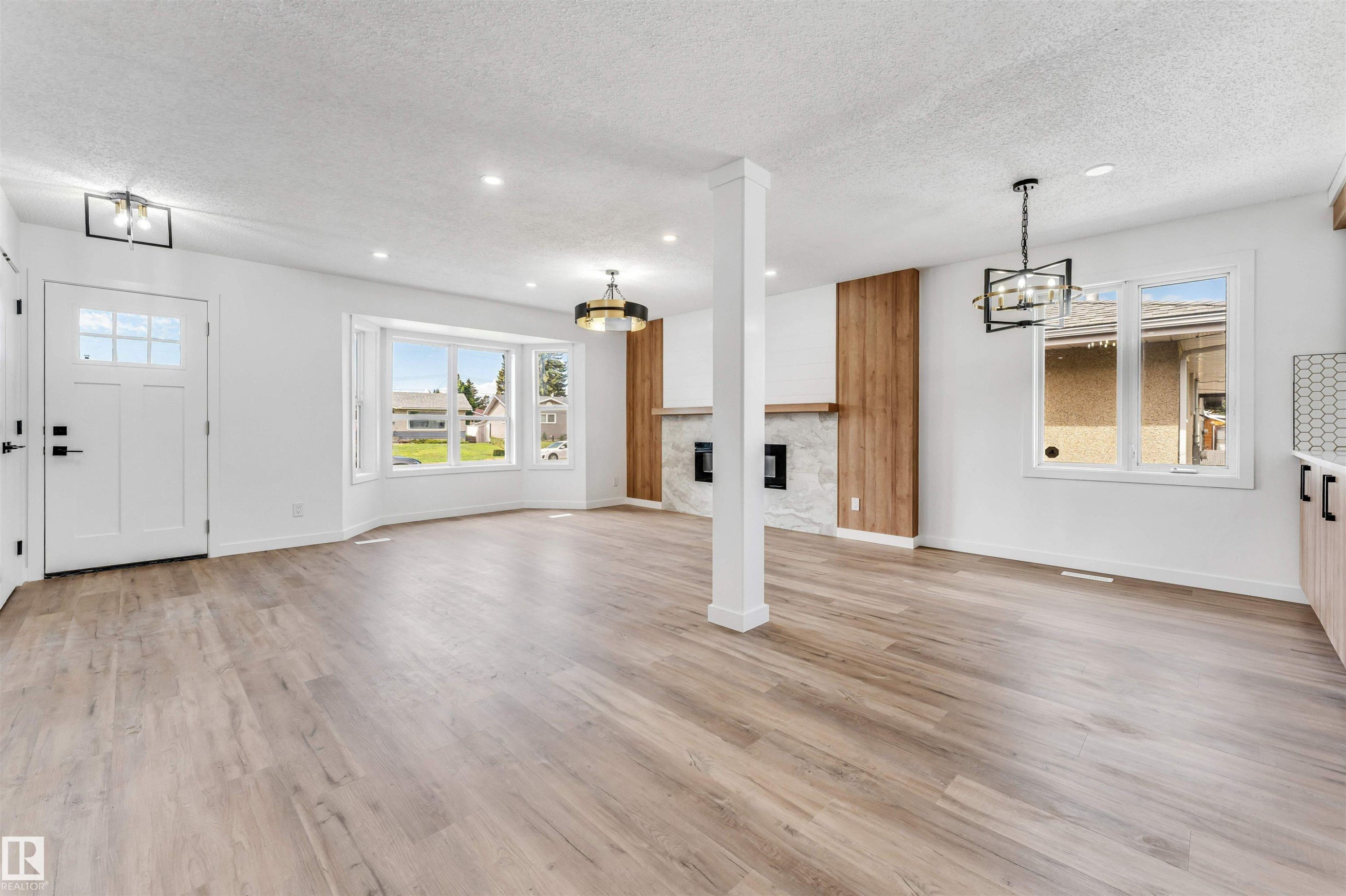 Spacious room featuring light wood-finish flooring, a contemporary fireplace with a stone surround and wood paneling, and an entry door with glass inserts - 6404 88 Avenue, Edmonton, AB
