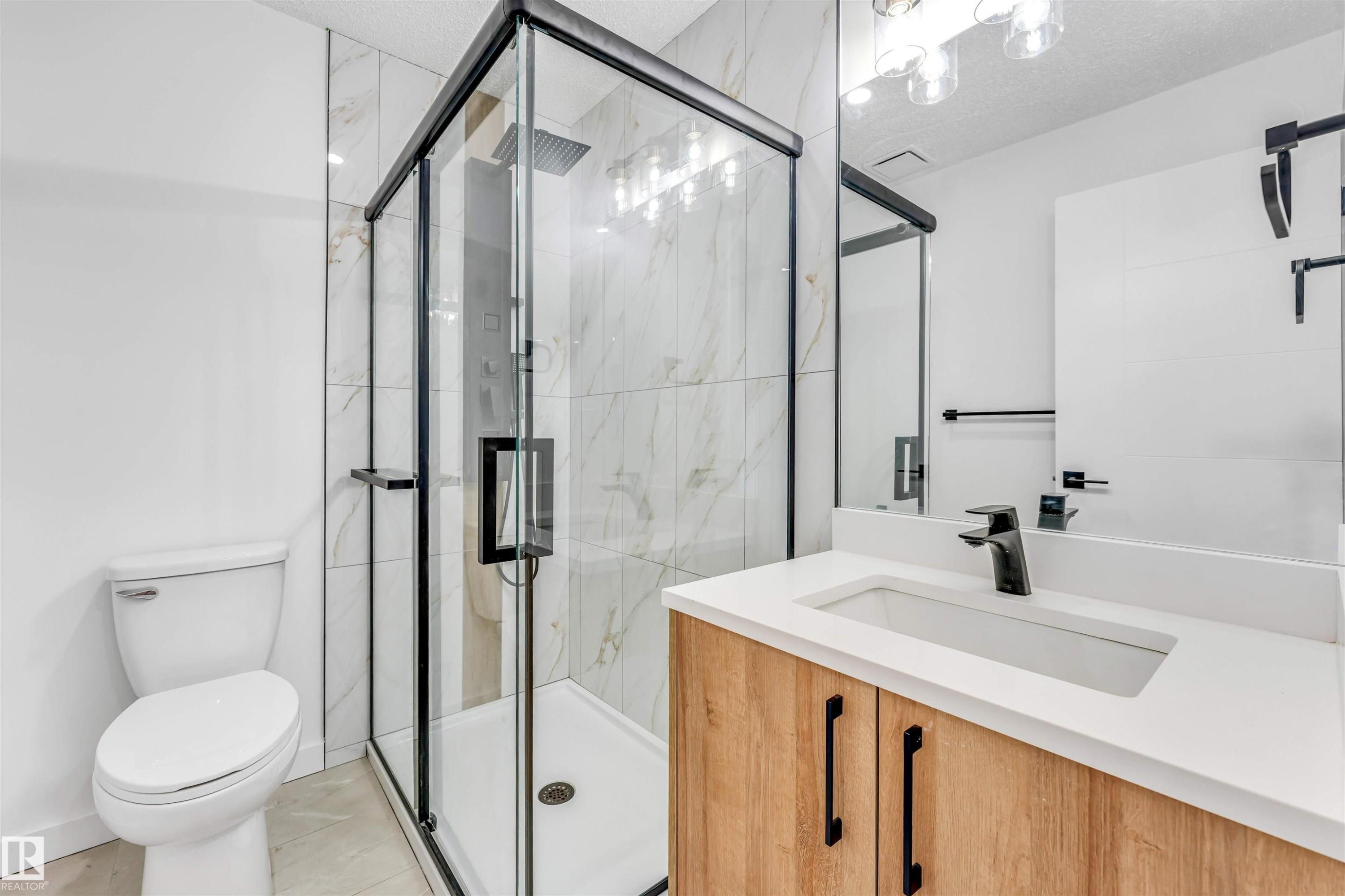 Contemporary bathroom featuring a glass-enclosed shower with black framing, white tile walls, a wood-finish vanity with a white countertop, and matte black fixtures - 6404 88 Avenue, Edmonton, AB