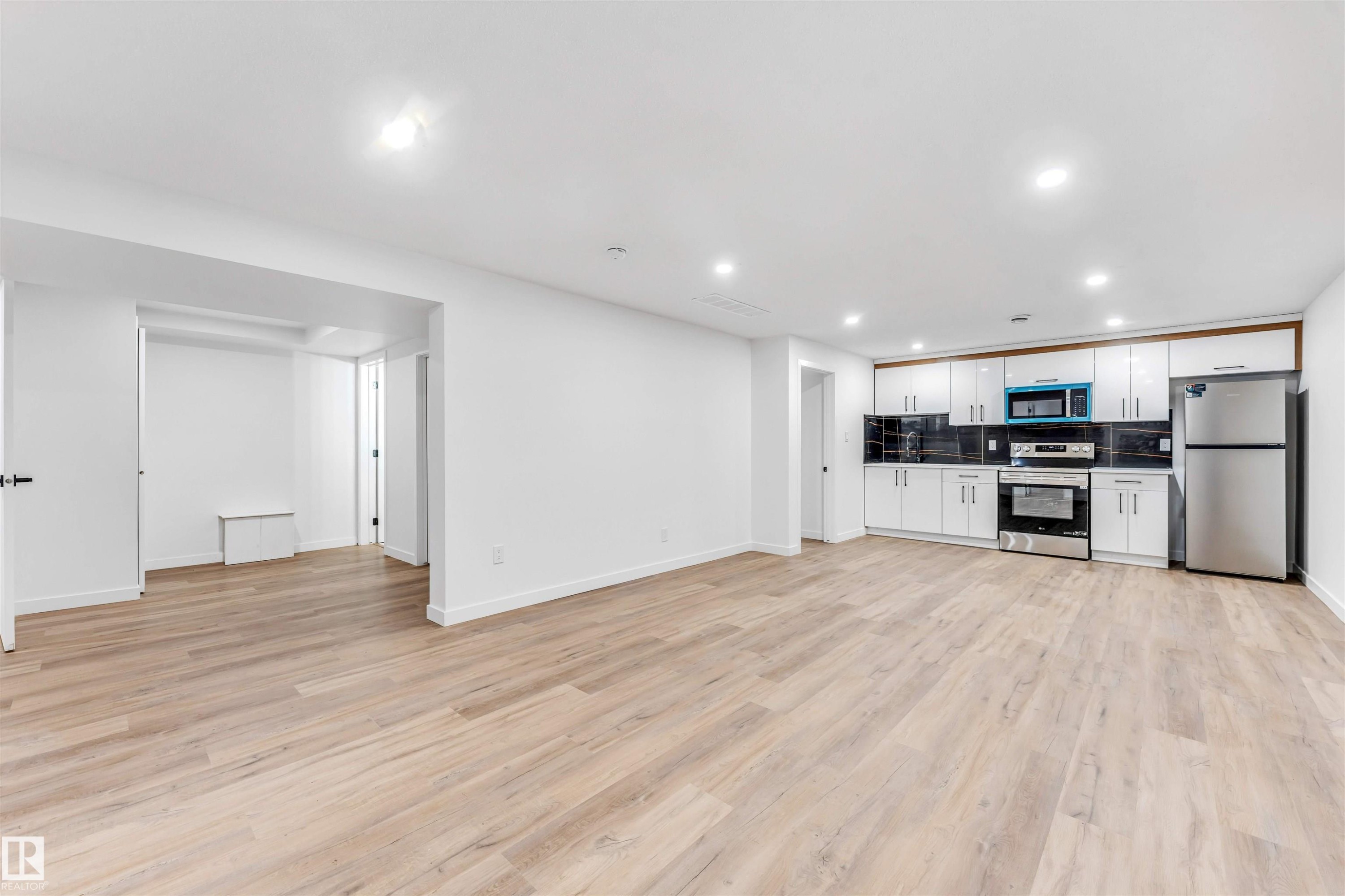 Open-concept living area featuring wood-finish flooring, recessed lighting, and a contemporary kitchen - 6404 88 Avenue, Edmonton, AB