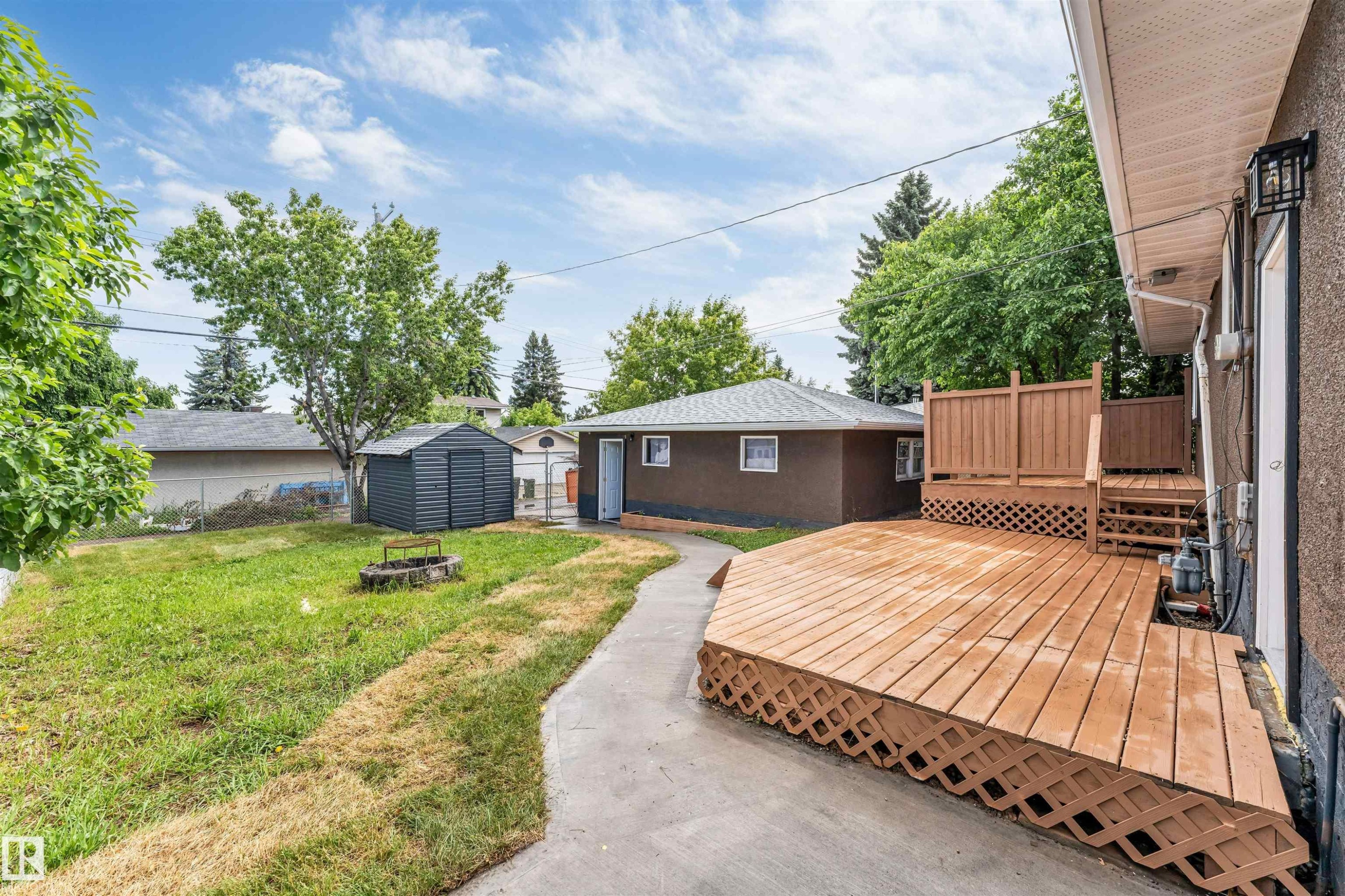 Spacious backyard featuring a multi-level wood deck with lattice skirting, concrete path, and a storage shed - 6404 88 Avenue, Edmonton, AB