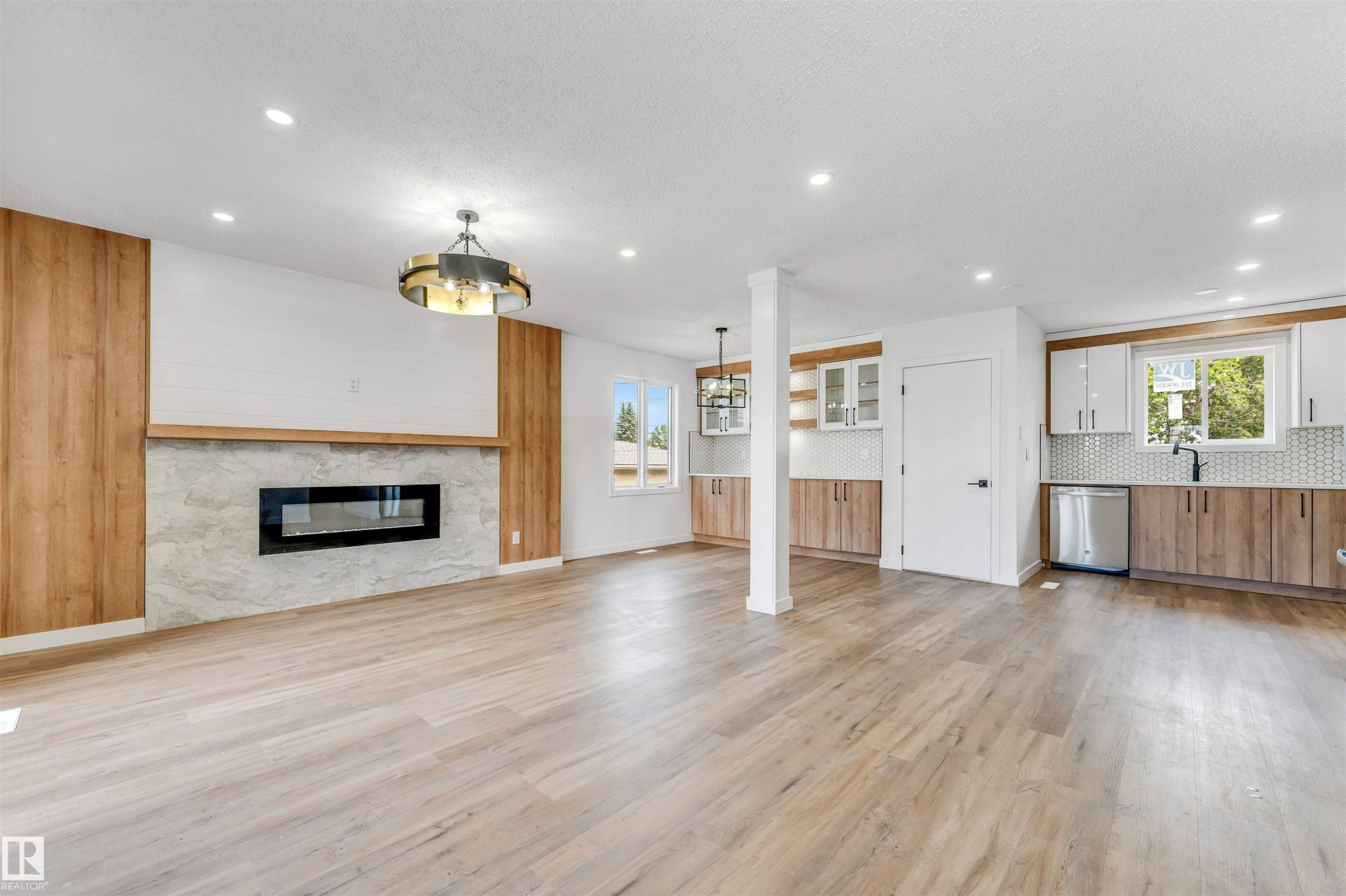 Open-concept living area featuring wood-finish flooring, a contemporary fireplace with a stone surround, and a wood mantel - 6404 88 Avenue, Edmonton, AB