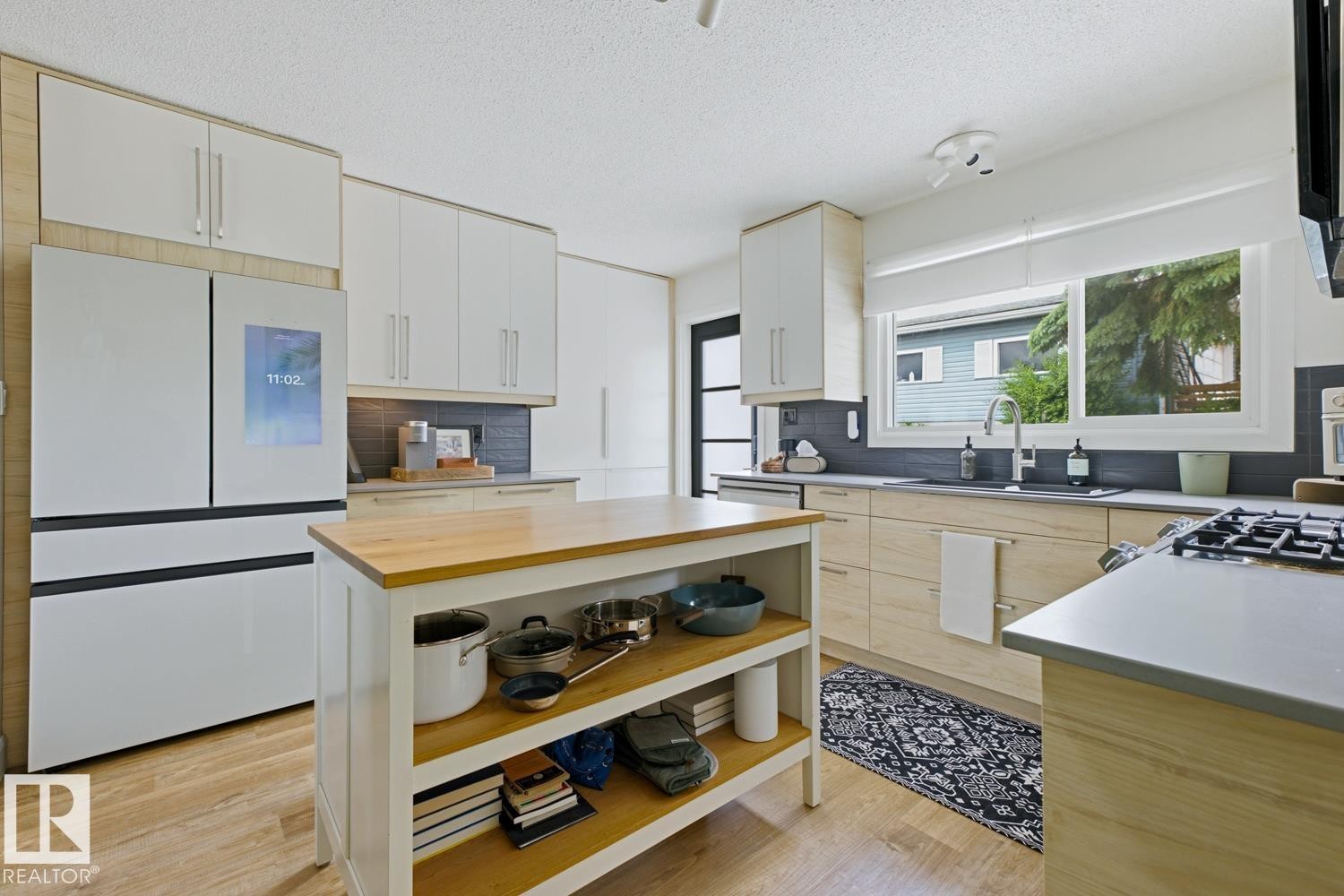 Well-appointed kitchen featuring a substantial central island with wood countertop, modern white upper cabinetry, and light wood-finish lower cabinetry - 3504 102 Avenue, Edmonton, AB