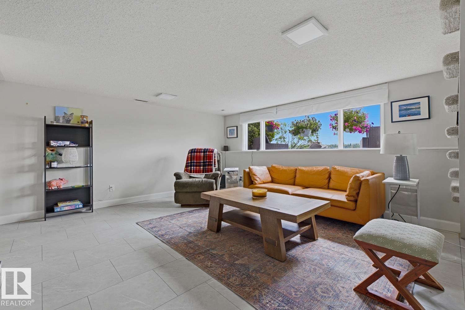 Spacious living area featuring light gray tile flooring and a bright window with exterior landscaping - 3504 102 Avenue, Edmonton, AB