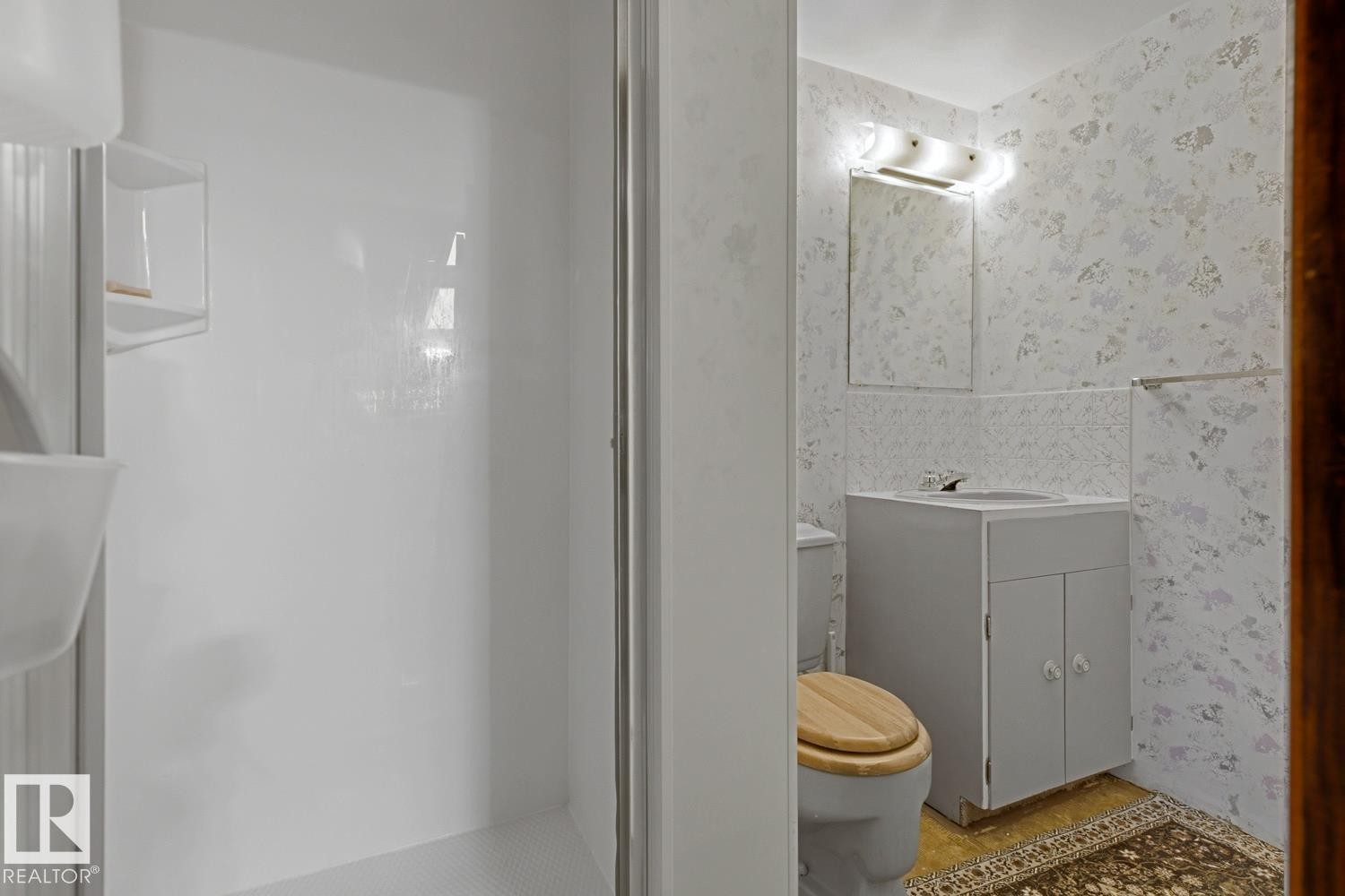 Bathroom featuring a white shower enclosure with built-in shelving, a vanity with a white cabinet, and a wall-mounted mirror with overhead lighting - 3504 102 Avenue, Edmonton, AB