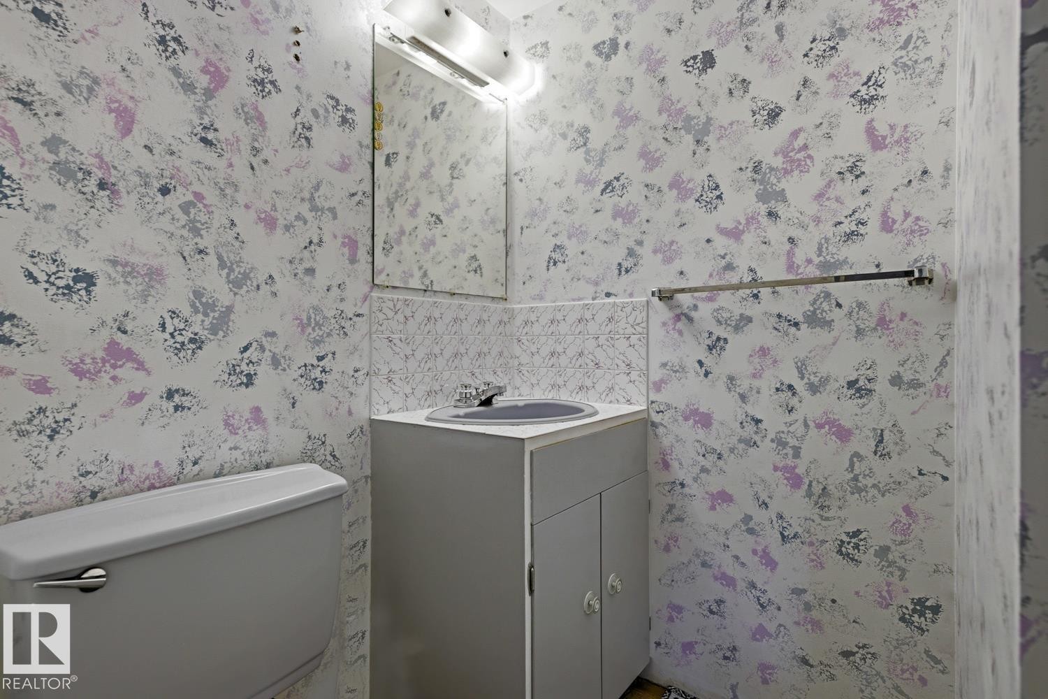 Compact bathroom featuring a white toilet, single vanity with a gray cabinet, and a wall-mounted mirror - 3504 102 Avenue, Edmonton, AB