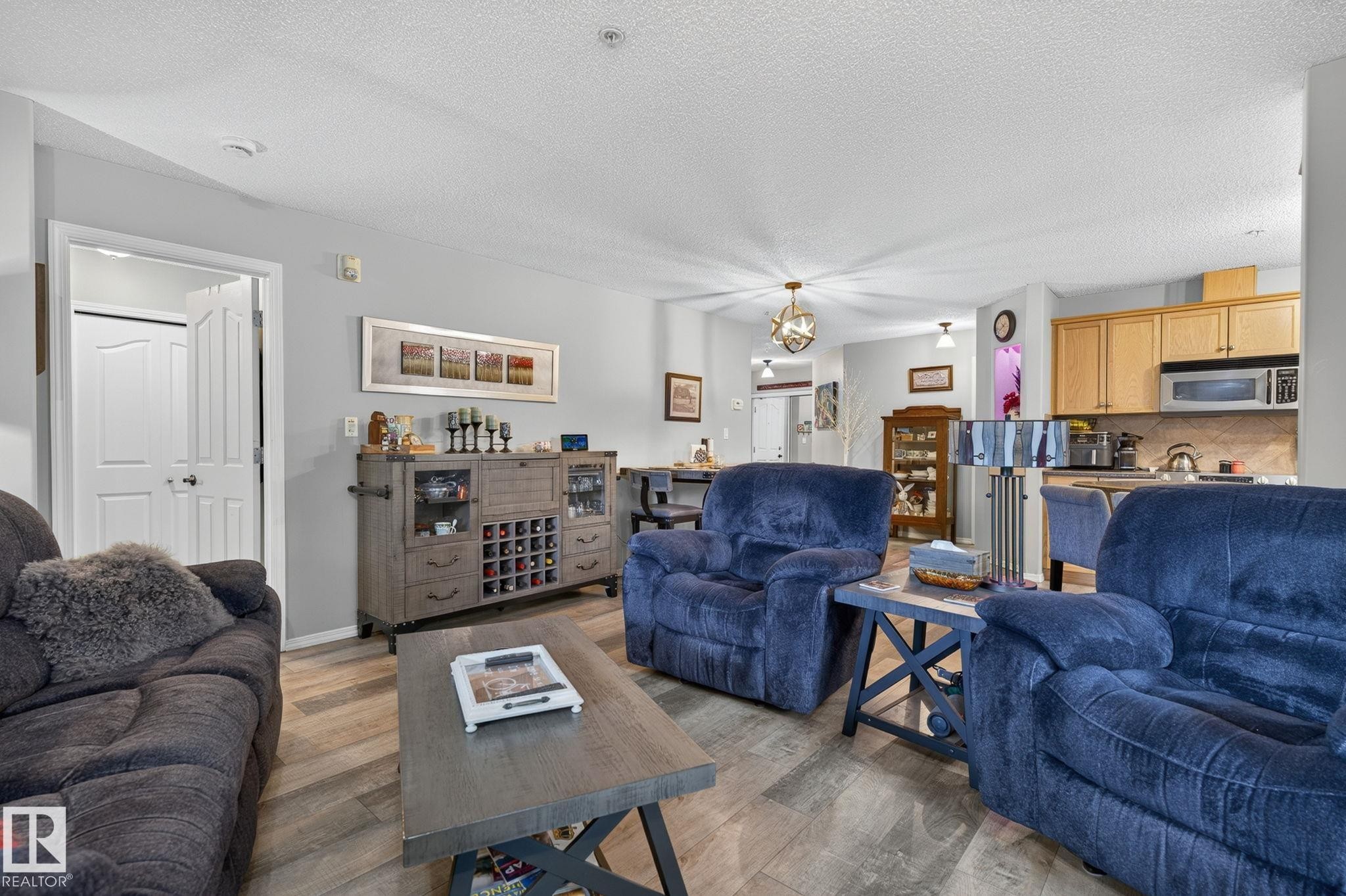 Open-concept living area featuring wood-finish flooring, light grey wall paint, and a textured ceiling - 122 279 Suder Greens Drive, Edmonton, AB