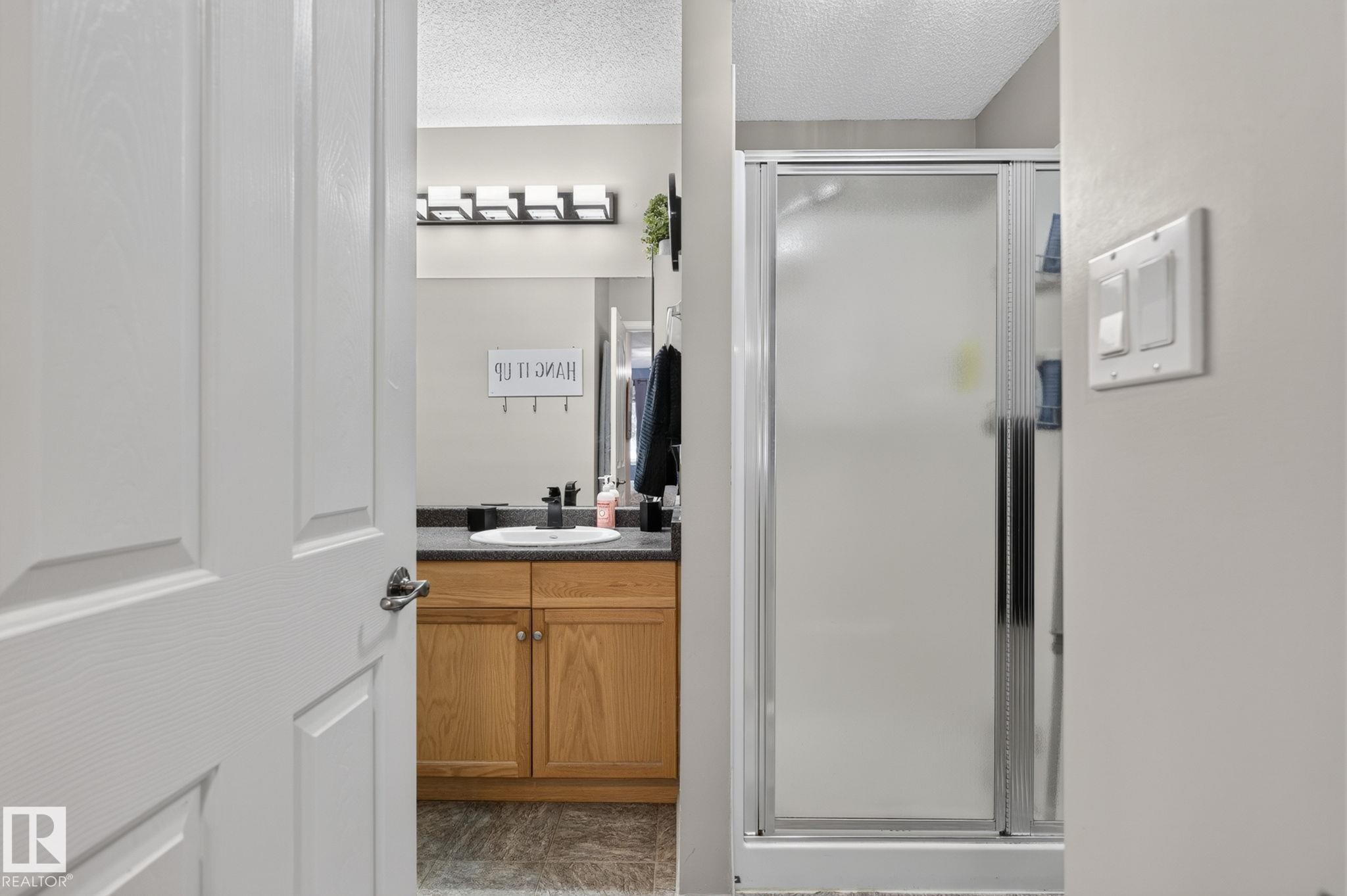 Bathroom featuring a wood-finish vanity with dark countertop, basin sink, and matte black faucet - 122 279 Suder Greens Drive, Edmonton, AB