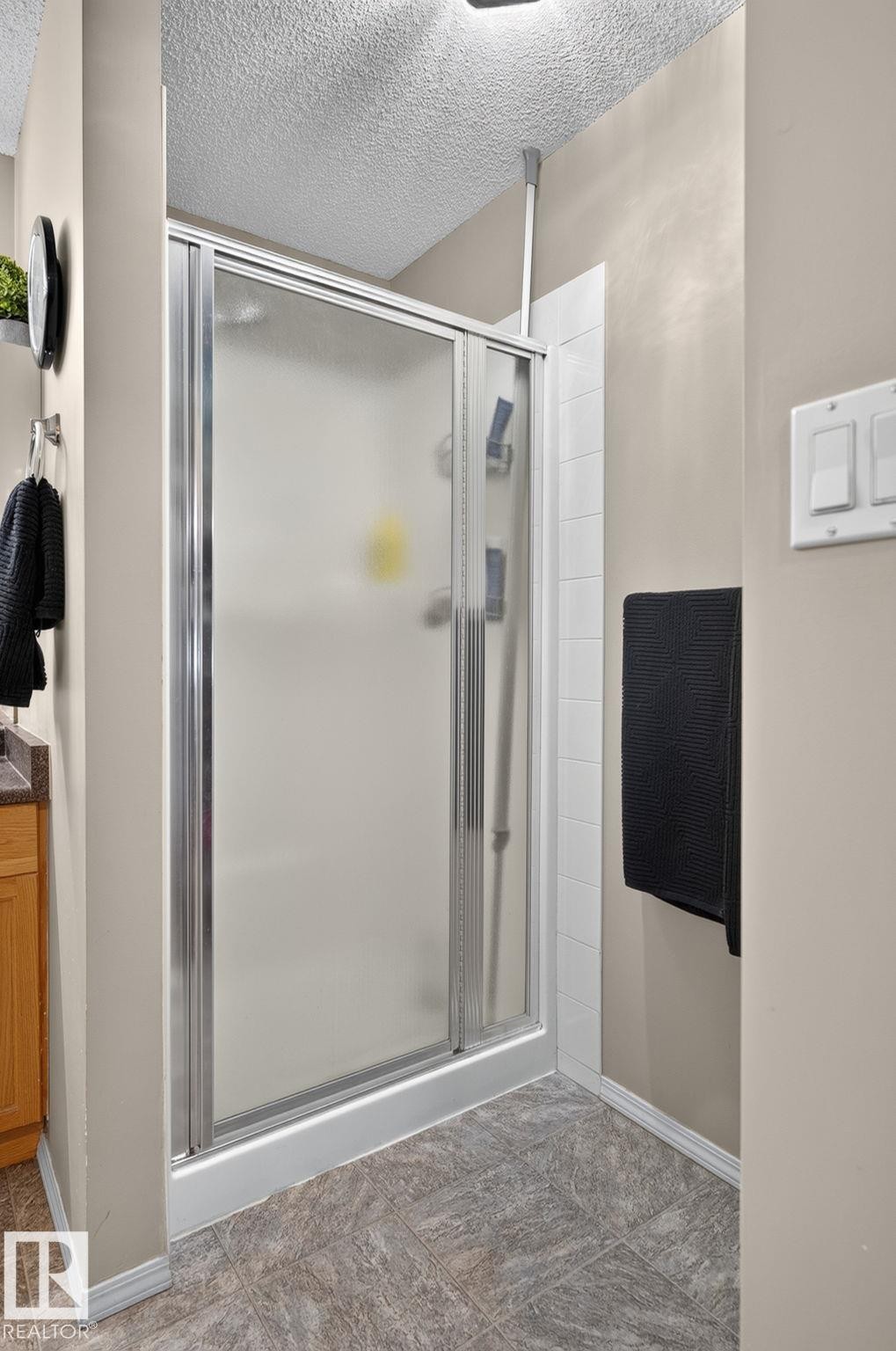 Enclosed shower with frosted glass and chrome framing, white tile surround, and textured ceiling - 122 279 Suder Greens Drive, Edmonton, AB