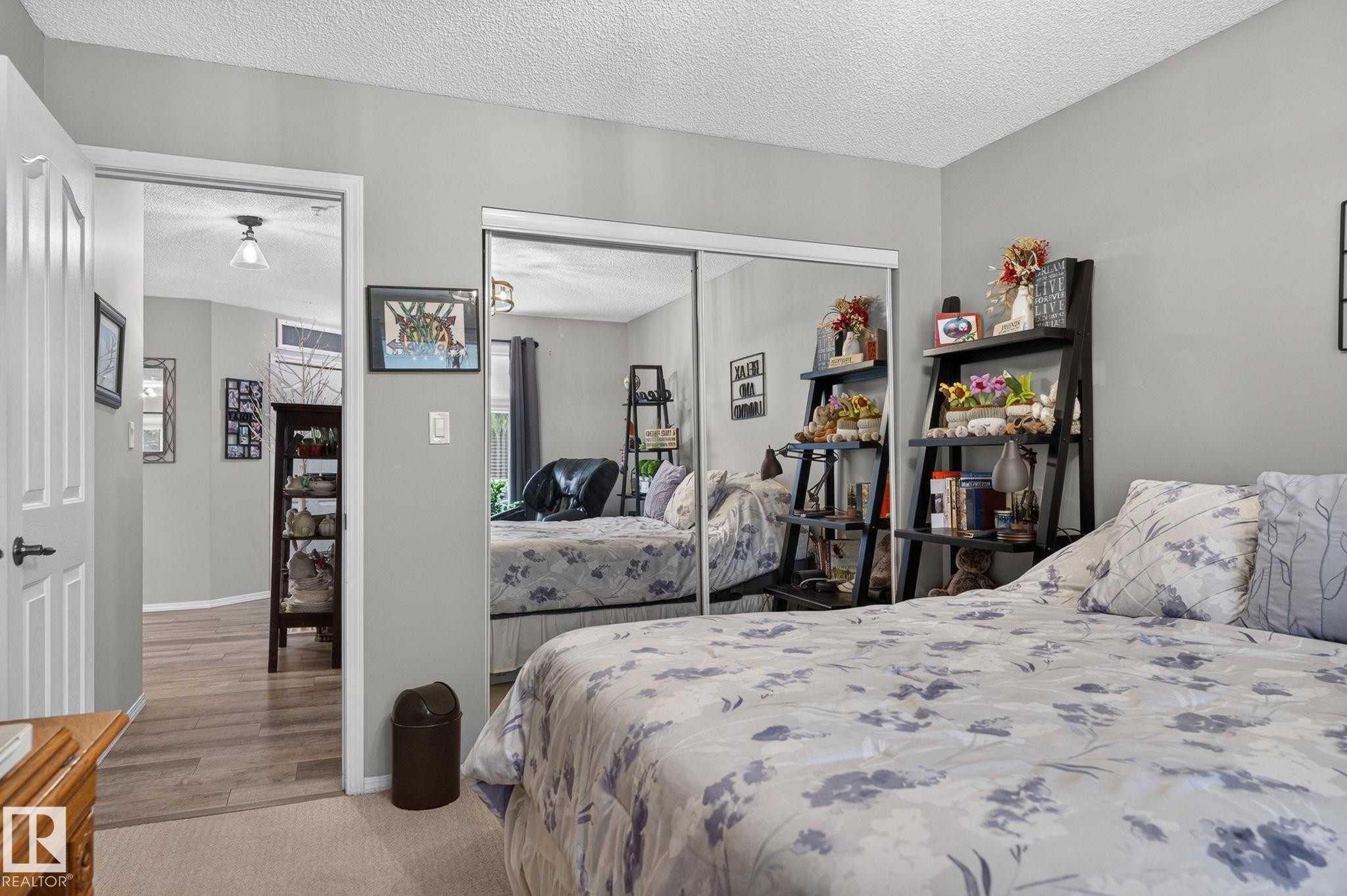 Bedroom featuring mirrored closet doors, neutral wall paint, and a textured ceiling - 122 279 Suder Greens Drive, Edmonton, AB