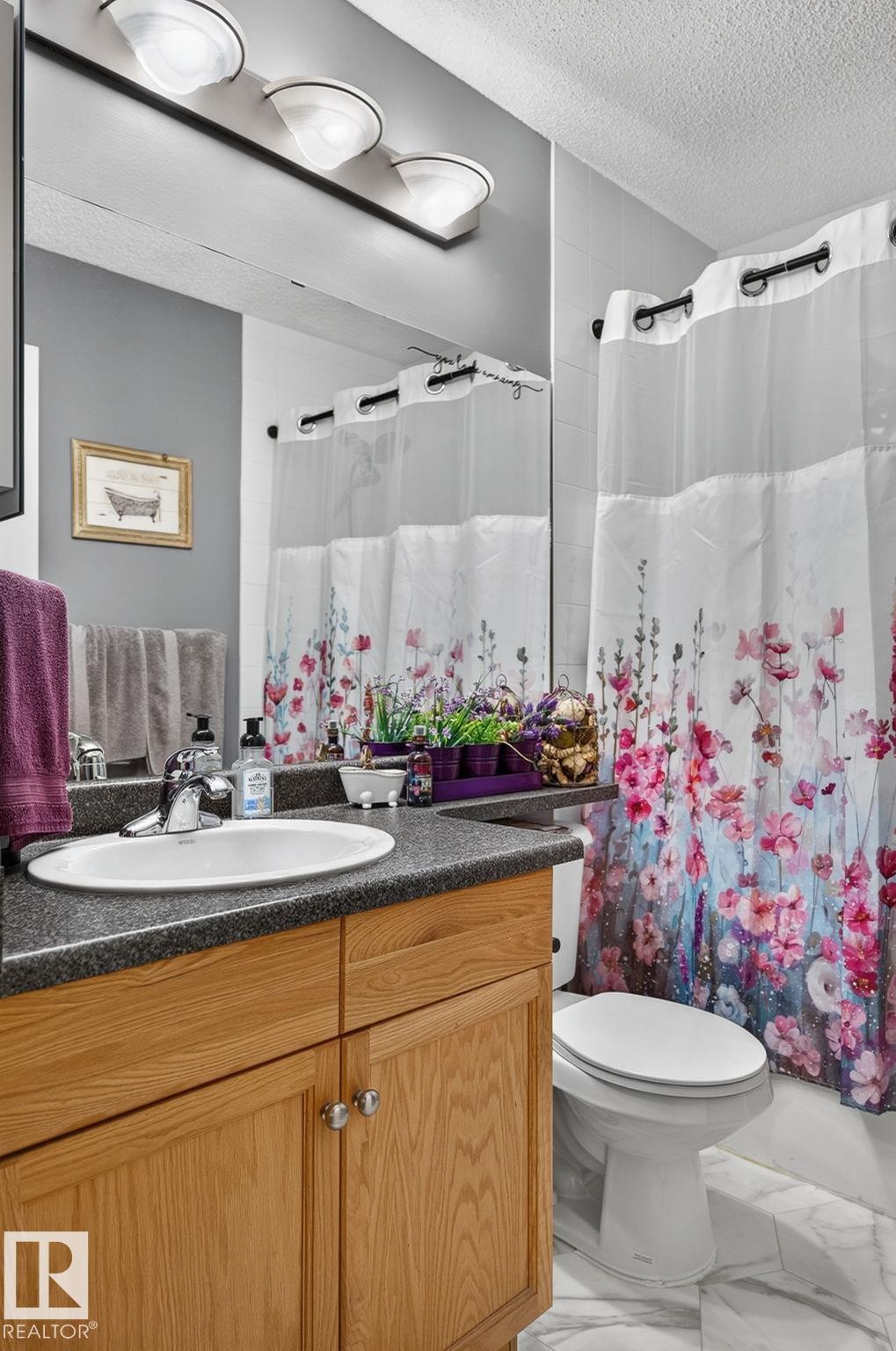Bathroom vanity with a white oval sink and chrome faucet, featuring a speckled dark countertop and light wood-finish cabinetry - 122 279 Suder Greens Drive, Edmonton, AB