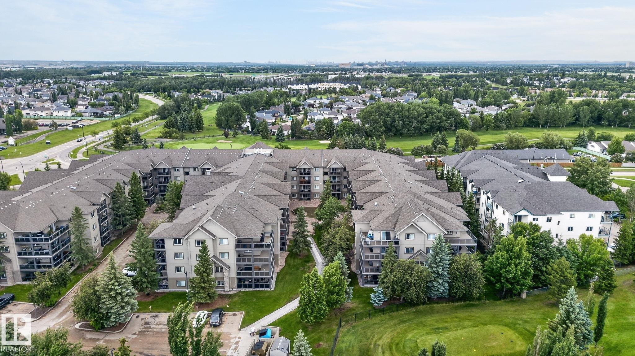 Expansive condominium complex featuring multiple buildings with private balconies, surrounded by mature evergreen and deciduous trees - 122 279 Suder Greens Drive, Edmonton, AB