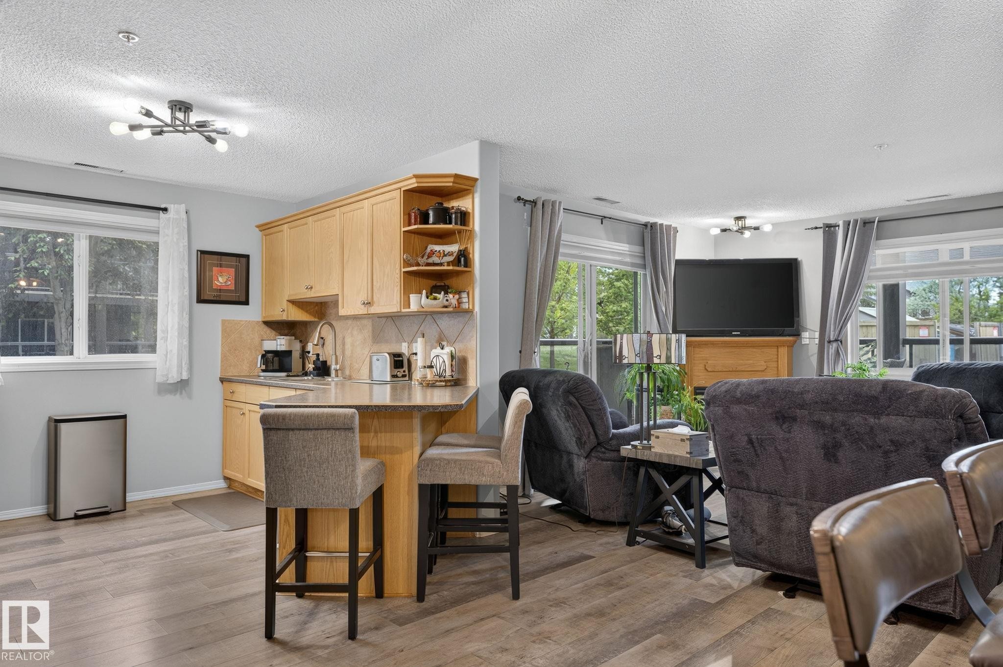 Open-concept living space featuring wood-finish flooring, a kitchen island with seating, natural wood cabinetry, a tiled backsplash, and recessed lighting - 122 279 Suder Greens Drive, Edmonton, AB