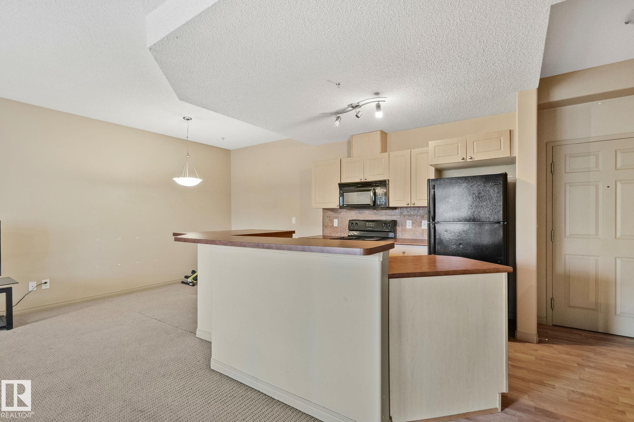 Kitchen area featuring light-toned cabinetry, a black refrigerator, and a built-in microwave - 209 5280 Terwillegar Boulevard, Edmonton, AB - Indoor Photo Showing Kitchen