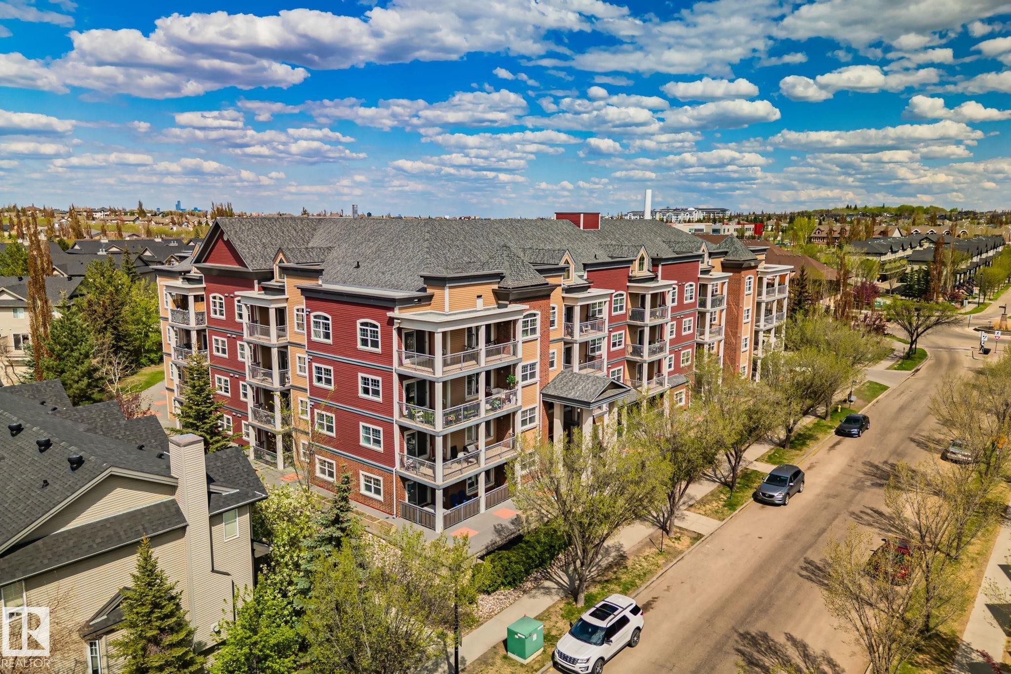 Multi-story building featuring a red and tan facade, multiple balconies with dark railings, and a dark shingled roof - 209 5280 Terwillegar Boulevard, Edmonton, AB - Outdoor With View
