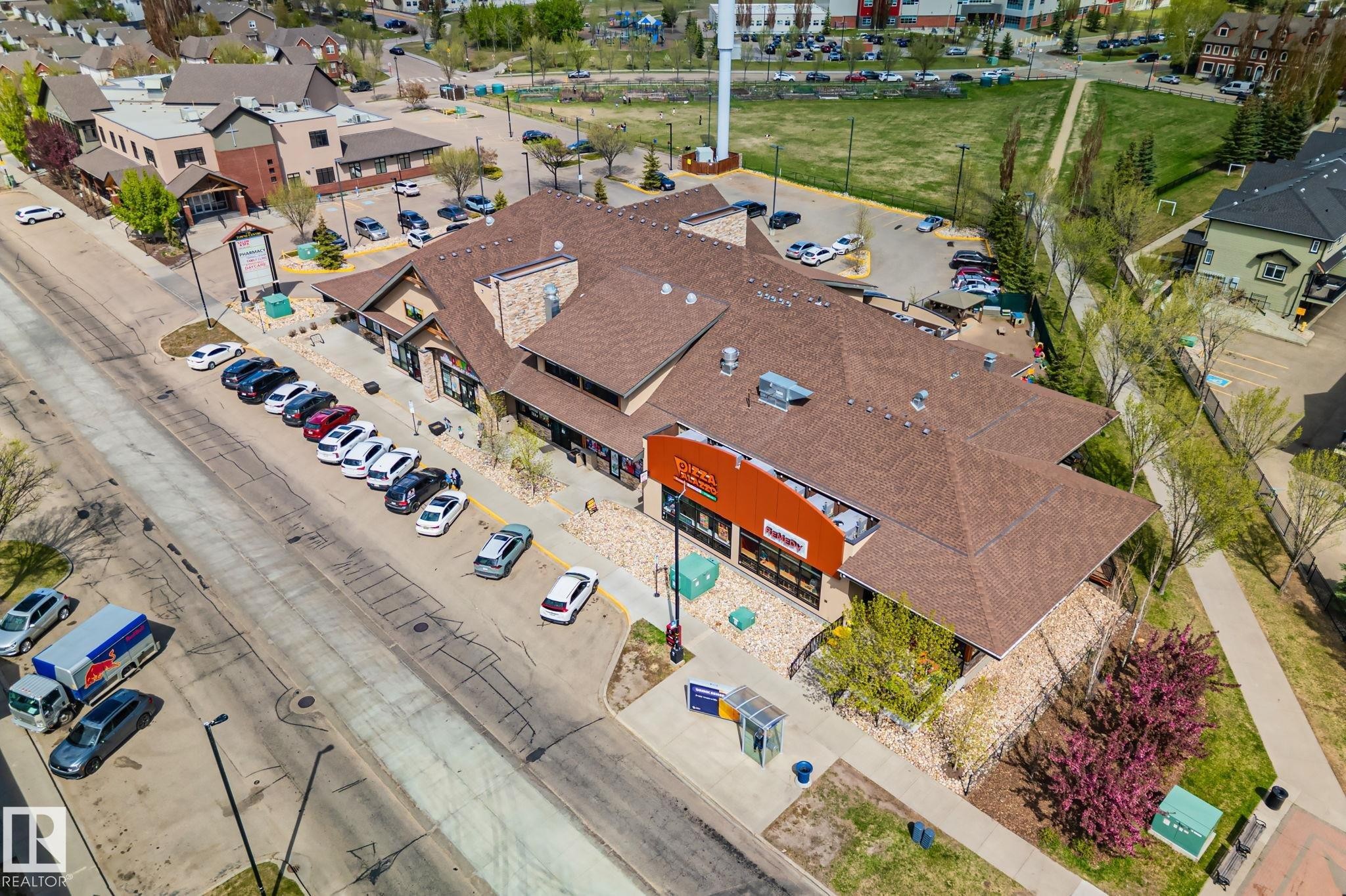 Commercial building featuring a shingled roof, stone facade accents, multiple tenant spaces, and ample surface parking - 209 5280 Terwillegar Boulevard, Edmonton, AB - Outdoor With View