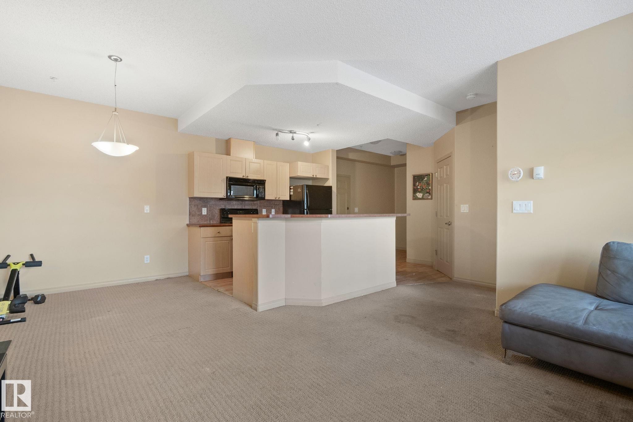Open-concept living space featuring a kitchen with light wood-finish cabinetry, black appliances, and a breakfast bar - 209 5280 Terwillegar Boulevard, Edmonton, AB - Indoor Photo Showing Kitchen