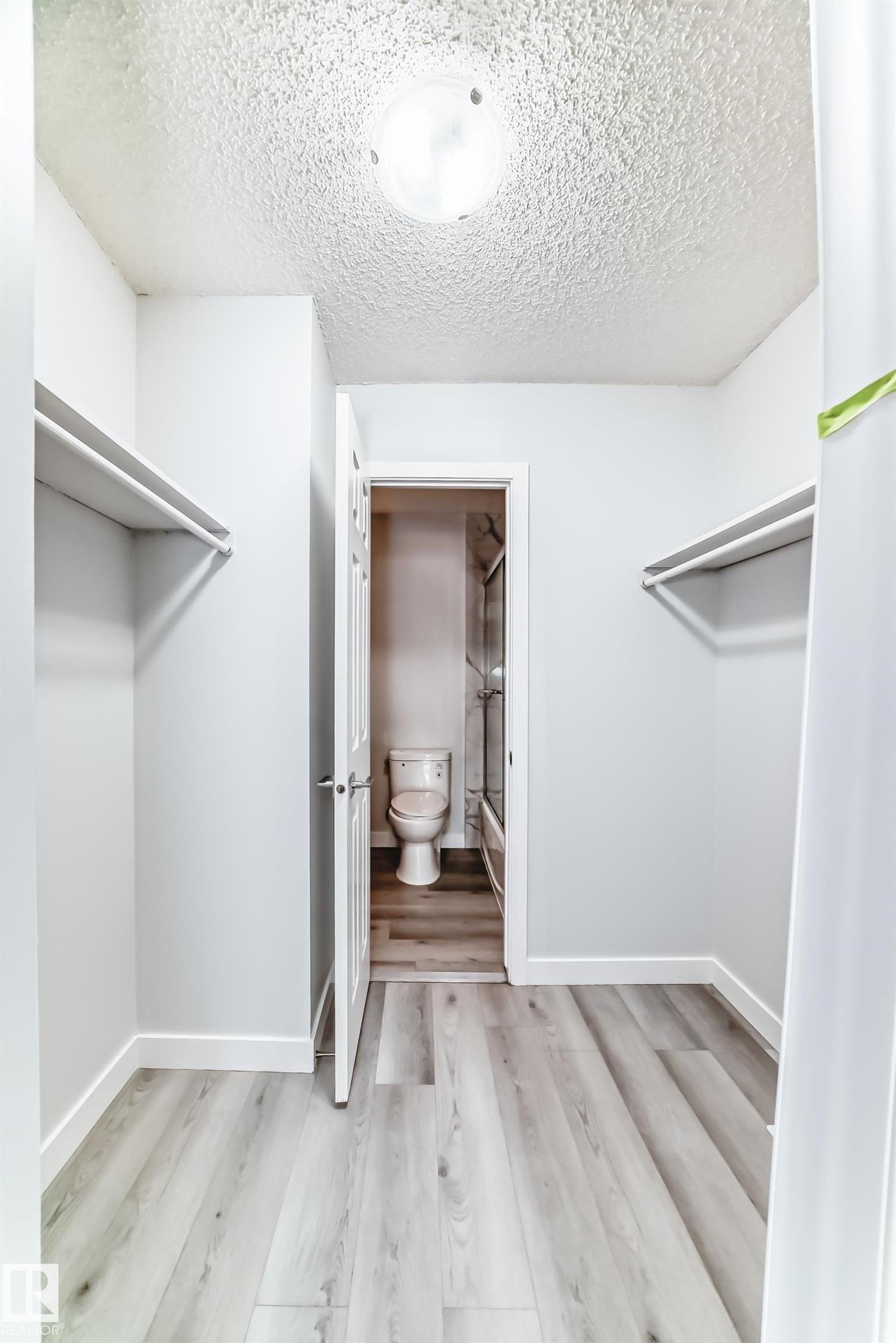 Walk-in closet featuring light wood-finish flooring, white walls, and built-in shelving - 23 1503 Mill Woods Road E, Edmonton, AB