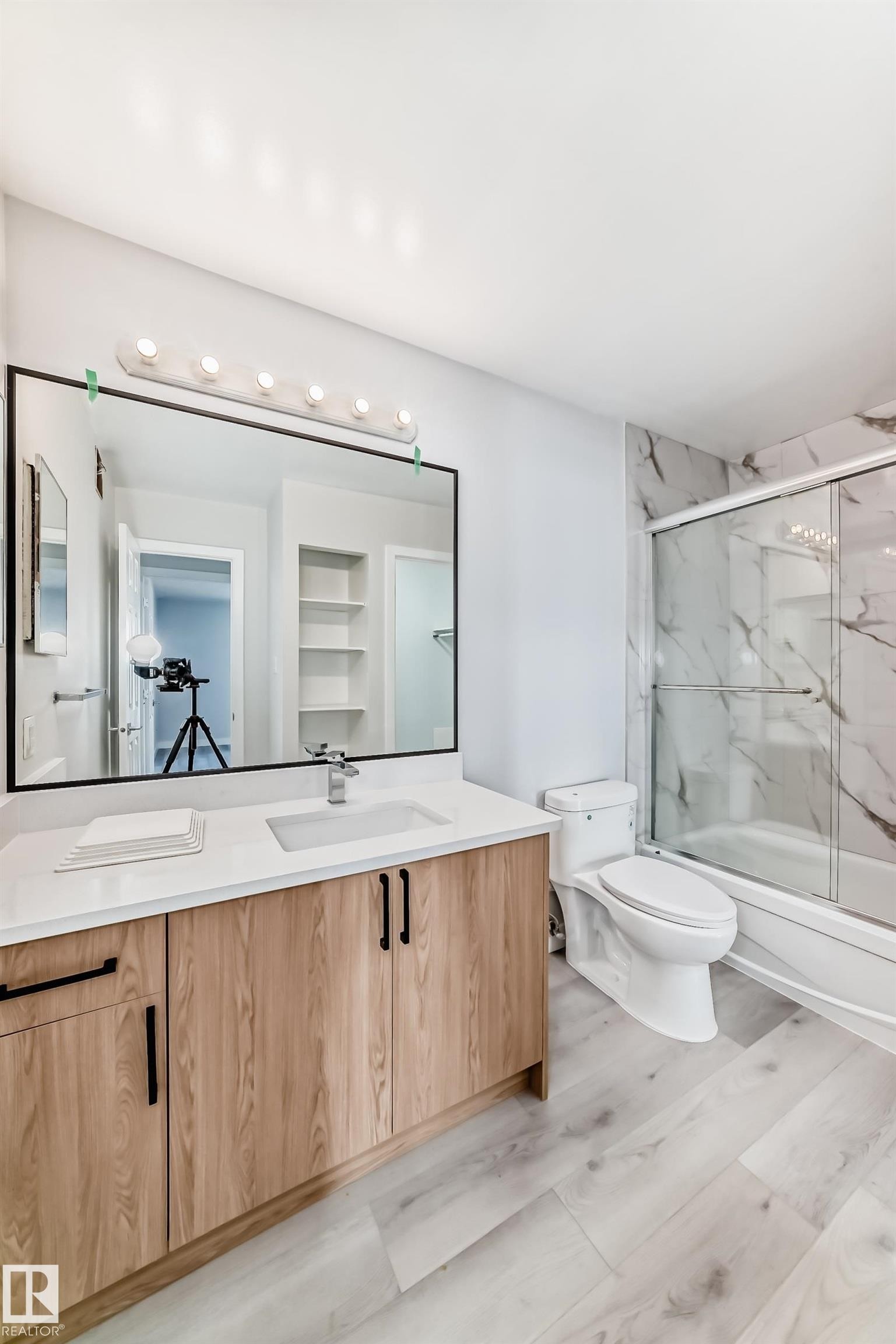 Bathroom featuring a wood-finish vanity with a white countertop, an undermount sink, and a large framed mirror - 23 1503 Mill Woods Road E, Edmonton, AB