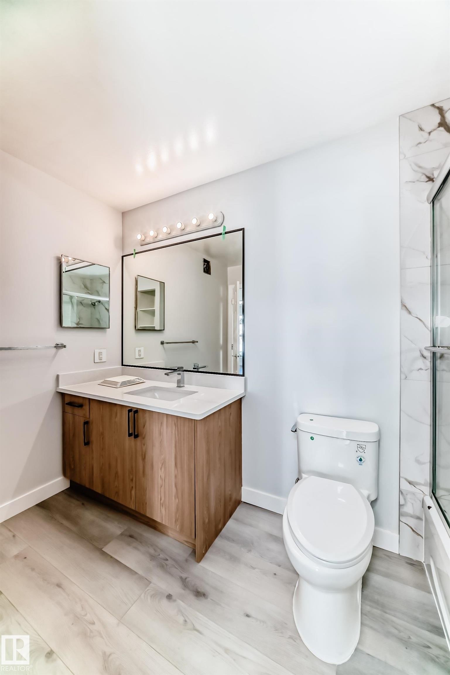 Modern vanity featuring wood-finish cabinetry, a white countertop, and an undermount sink - 23 1503 Mill Woods Road E, Edmonton, AB