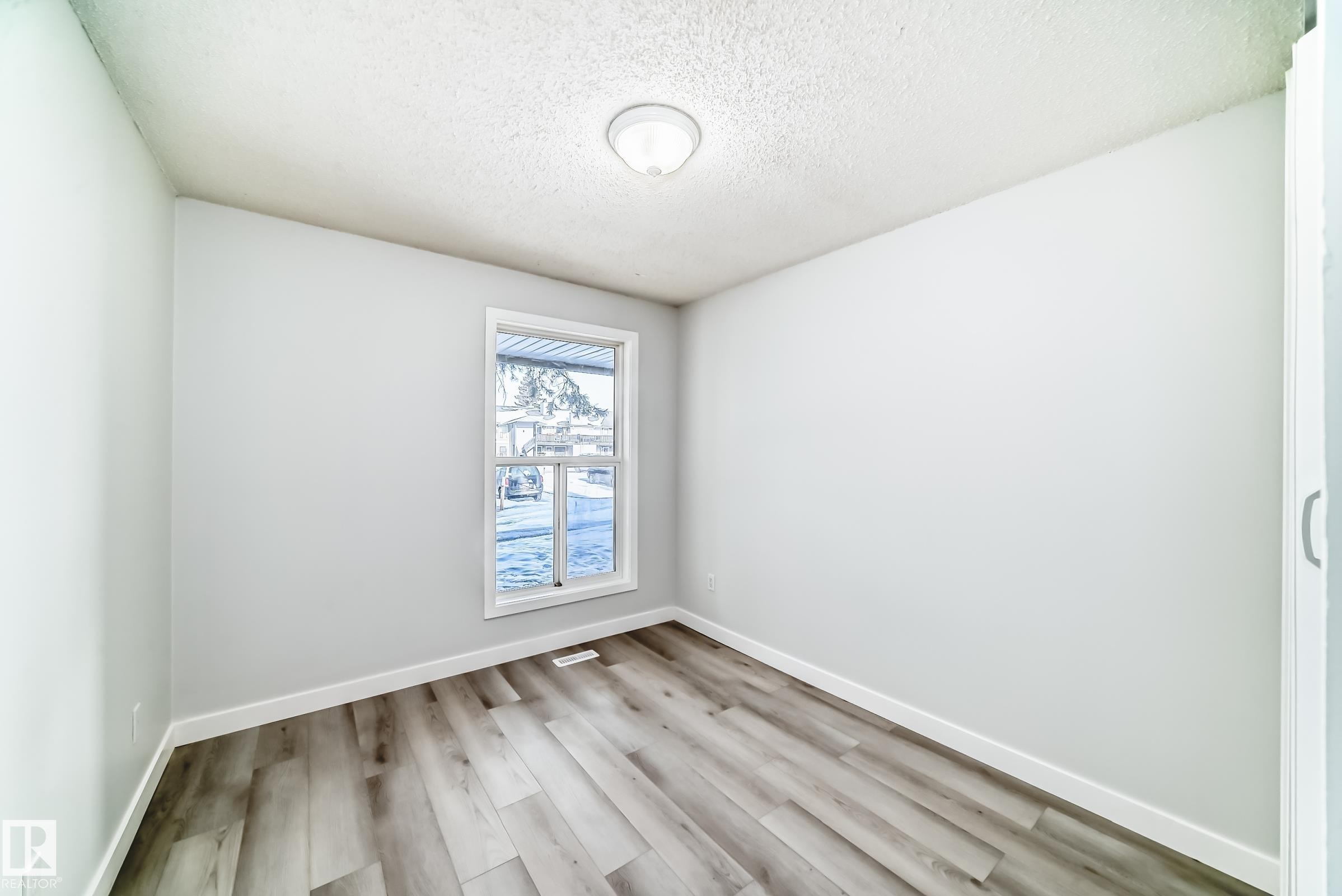 Room featuring wood-finish flooring, white baseboards, a white window frame, and a flush-mount ceiling light fixture - 23 1503 Mill Woods Road E, Edmonton, AB