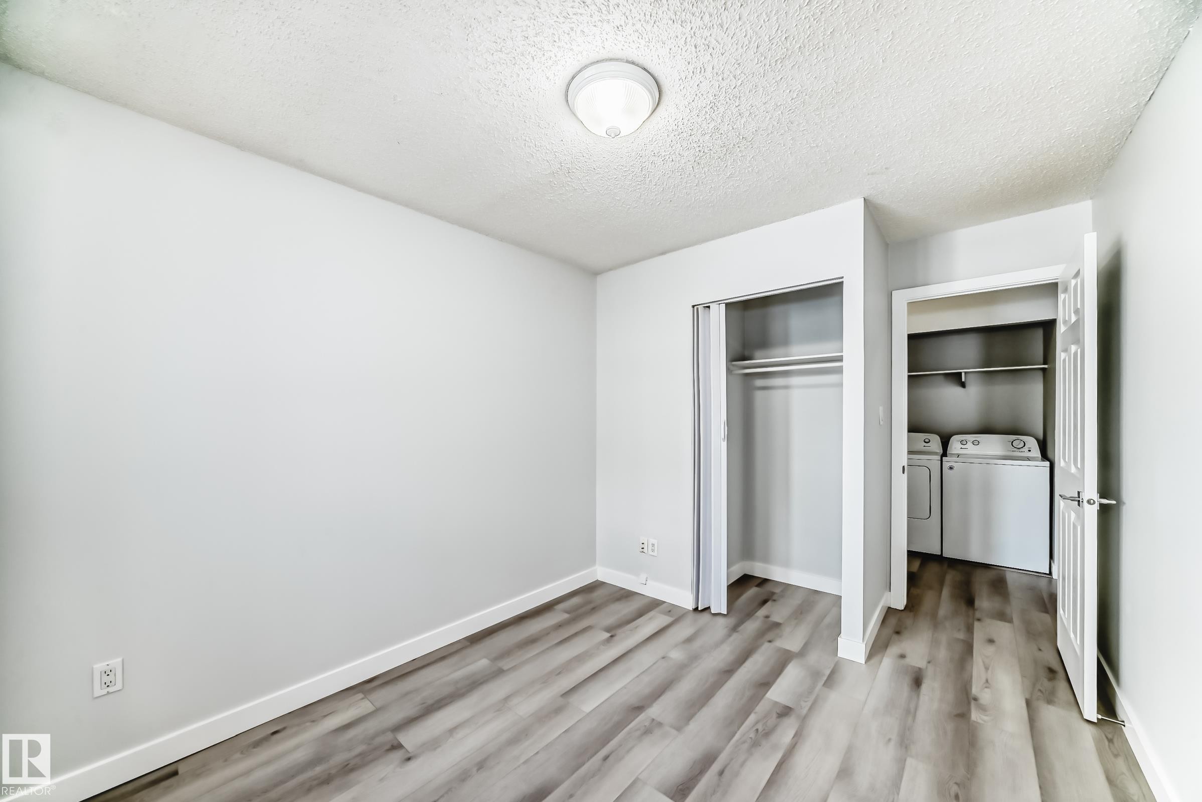 Light-filled room featuring wood-finish flooring, a flush-mount ceiling light, and white baseboards - 23 1503 Mill Woods Road E, Edmonton, AB