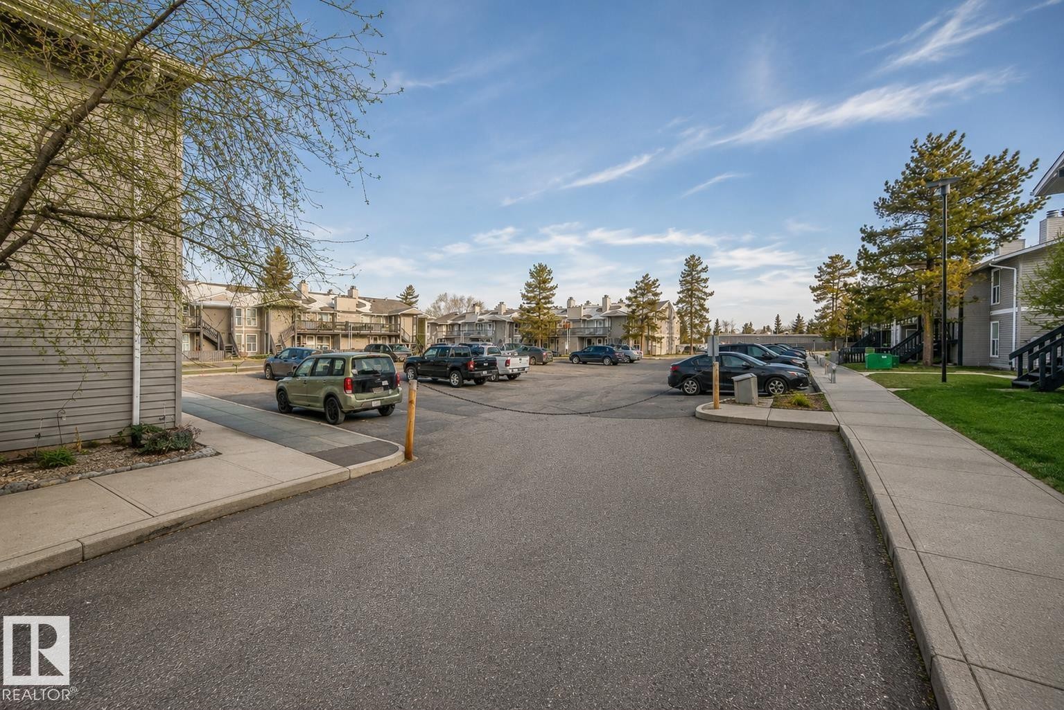Paved parking lot with designated spaces, concrete sidewalks, and surrounding mature trees - 23 1503 Mill Woods Road E, Edmonton, AB