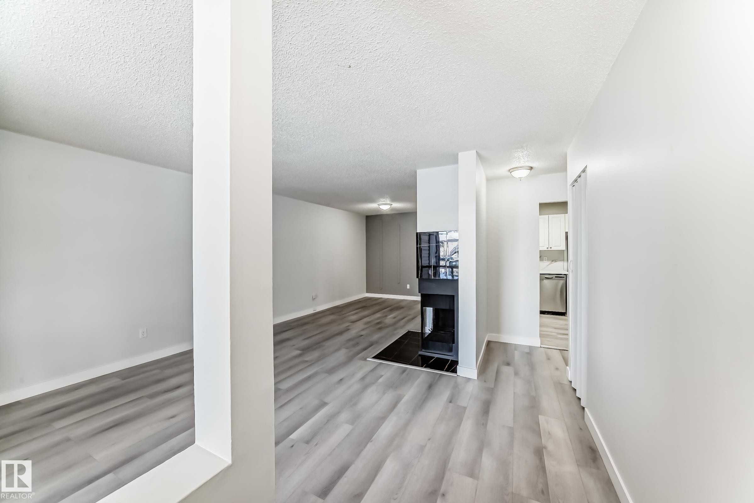 Interior living space with wood-finish flooring, a built-in fireplace, and white painted walls - 23 1503 Mill Woods Road E, Edmonton, AB