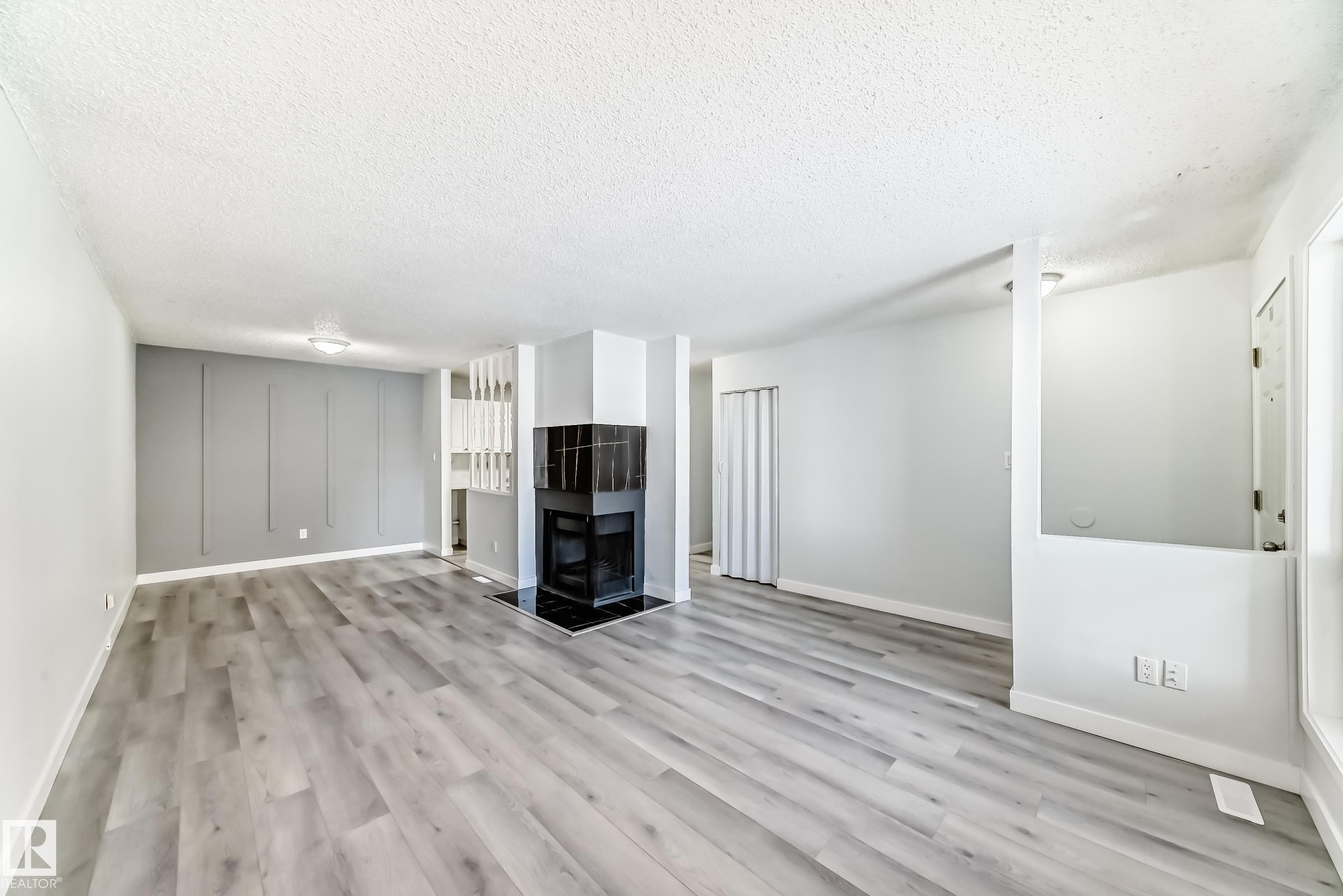 Spacious living area featuring wood-finish flooring, a black-tiled fireplace with hearth, and a decorative accent wall - 23 1503 Mill Woods Road E, Edmonton, AB