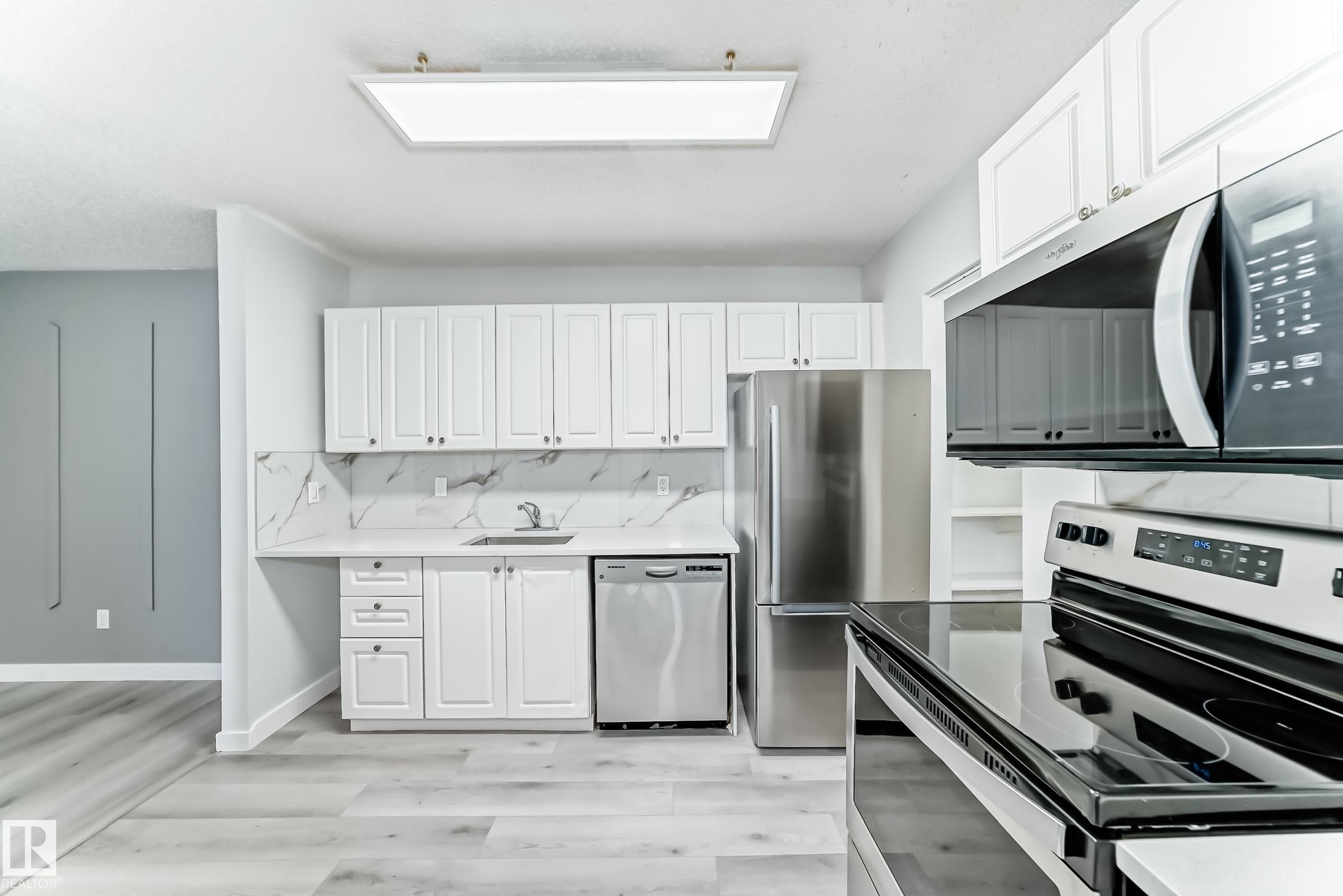 Kitchen featuring white cabinetry, stone-look countertops, stainless steel appliances, and wood-finish flooring - 23 1503 Mill Woods Road E, Edmonton, AB