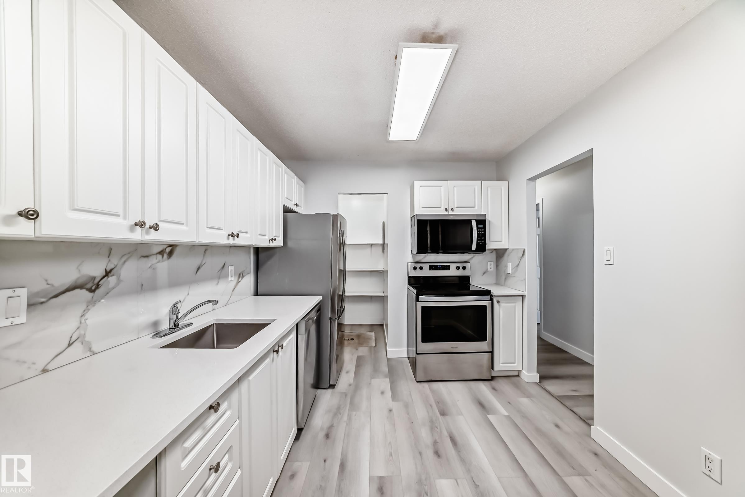 Kitchen featuring white shaker cabinetry, stainless steel appliances, light wood-finish flooring, and a marble-patterned backsplash - 23 1503 Mill Woods Road E, Edmonton, AB