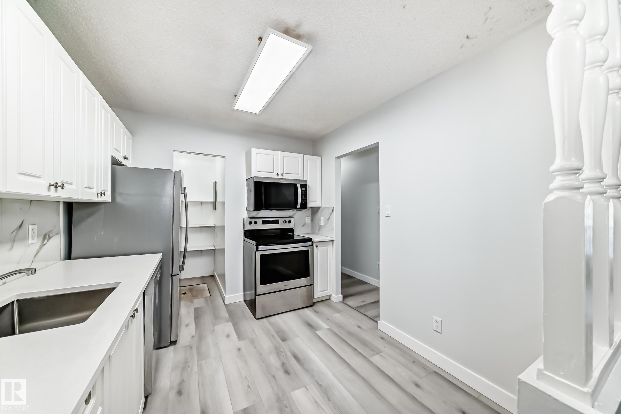Kitchen featuring white cabinetry, stainless steel appliances, light-toned wood-finish flooring, and a stone-look backsplash - 23 1503 Mill Woods Road E, Edmonton, AB