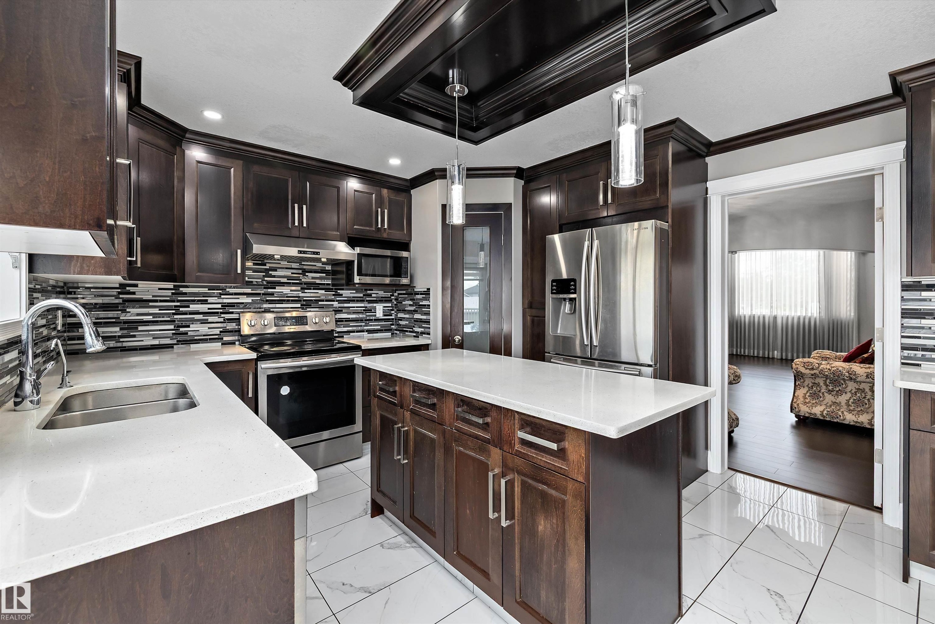 Kitchen featuring dark wood cabinetry, stainless steel appliances, a center island with a light-toned countertop, a multi-toned mosaic tile backsplash, and recessed lighting - 4831 154 Avenue, Edmonton, AB