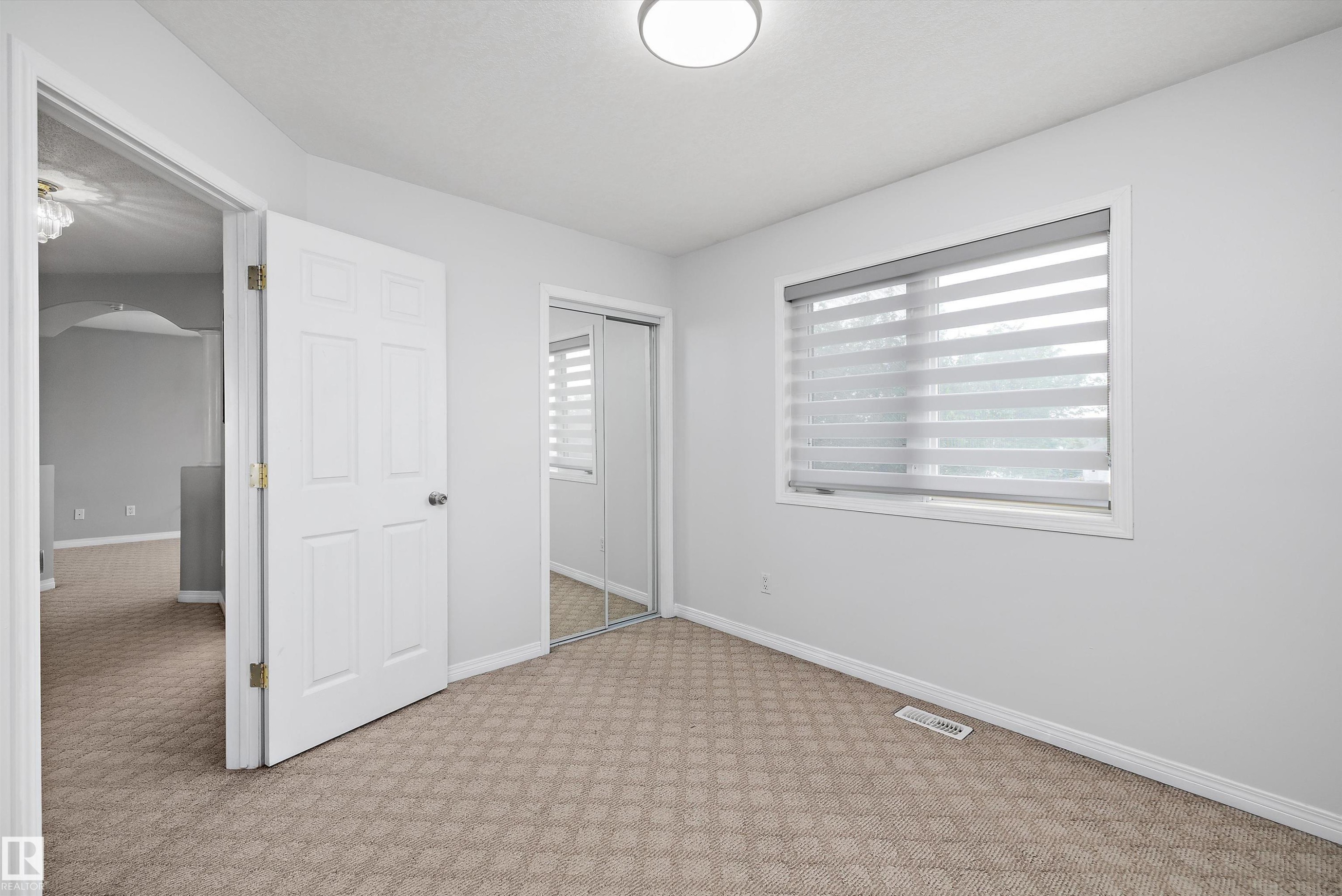 Bright room featuring patterned carpeting, a large window with horizontal blinds, and a mirrored closet - 4831 154 Avenue, Edmonton, AB
