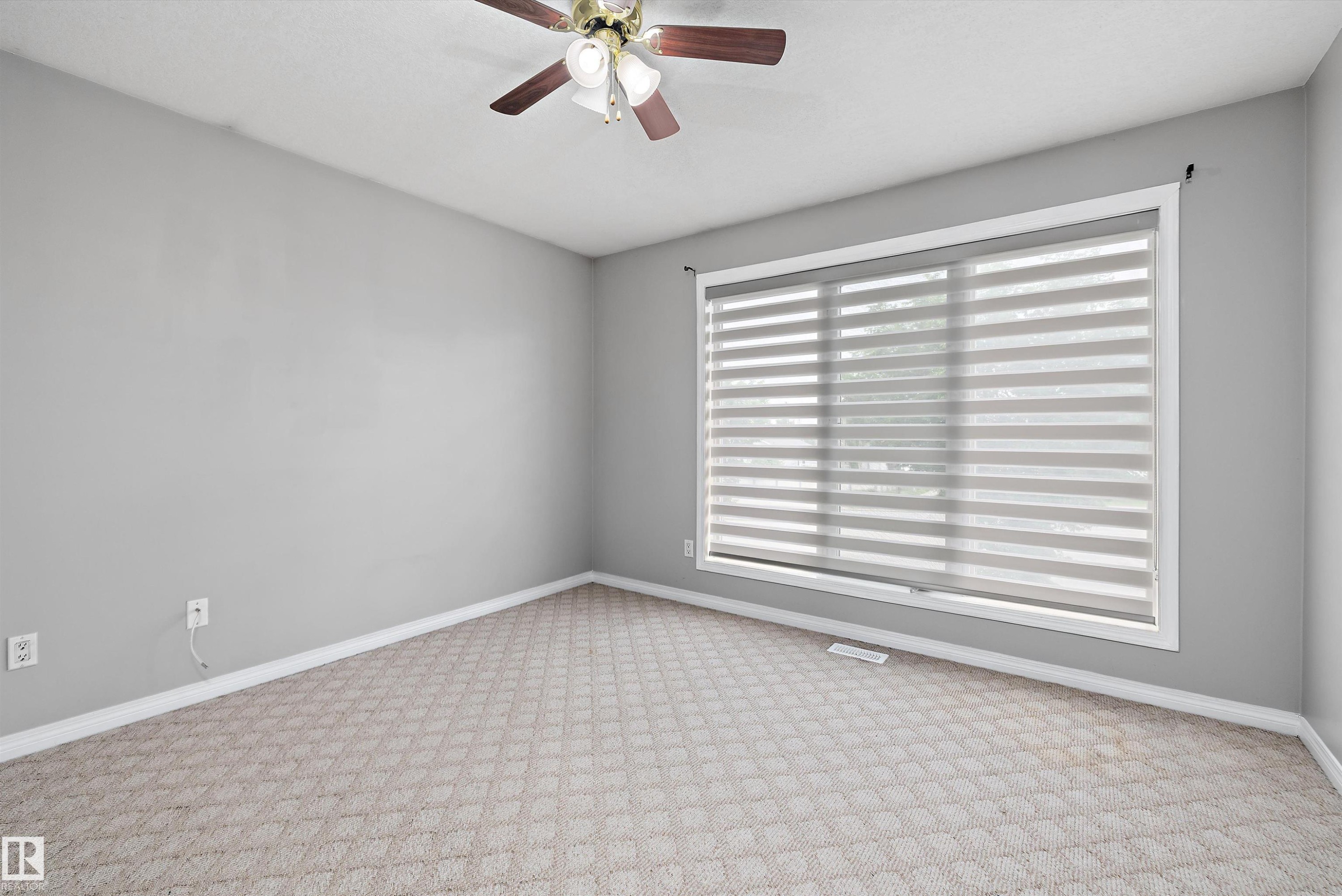 Spacious room featuring patterned carpet flooring, a ceiling fan with light fixture, and a large window with layered blinds - 4831 154 Avenue, Edmonton, AB