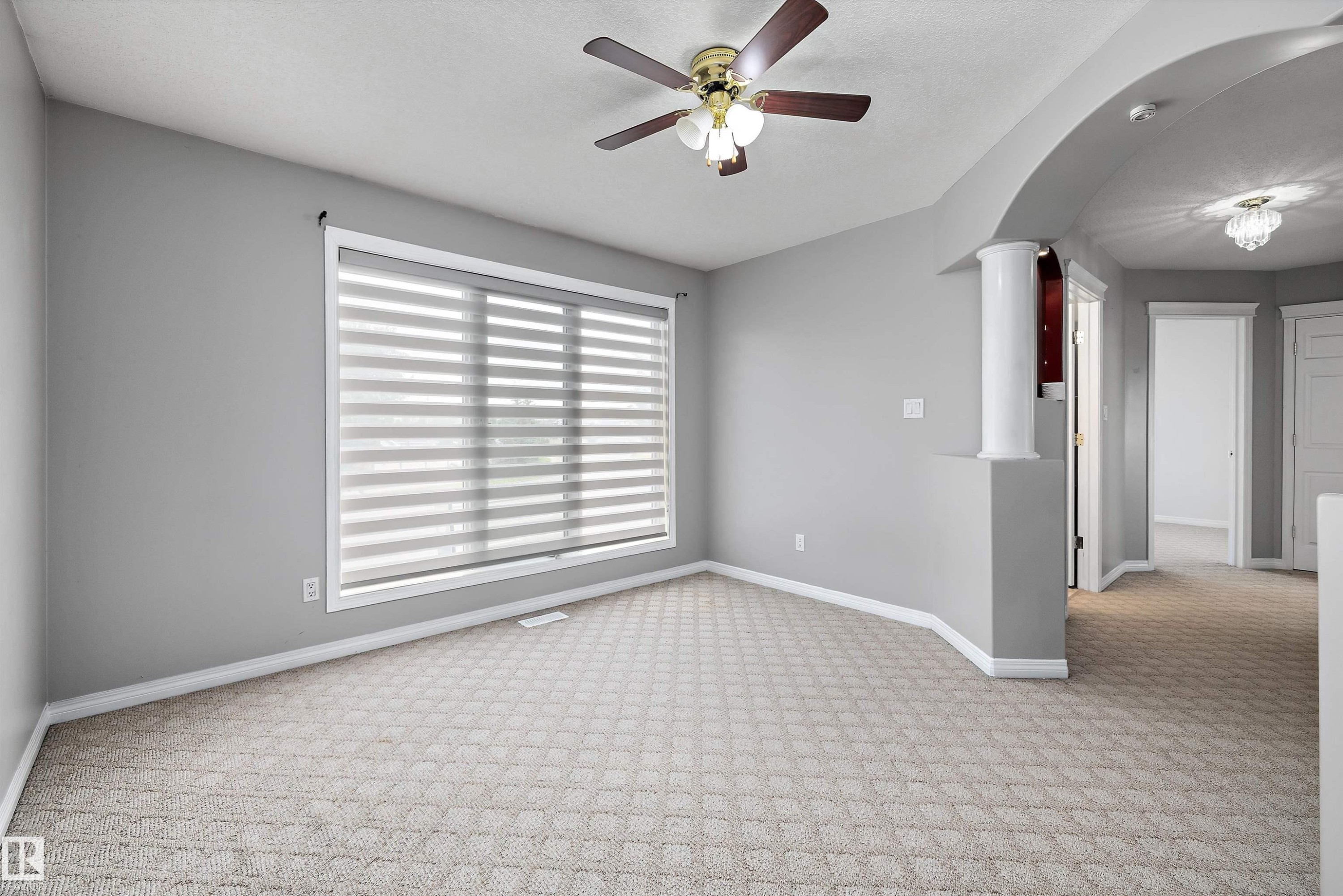 Carpeted room featuring a large window with horizontal blinds, a ceiling fan with light fixture, and an arched doorway - 4831 154 Avenue, Edmonton, AB