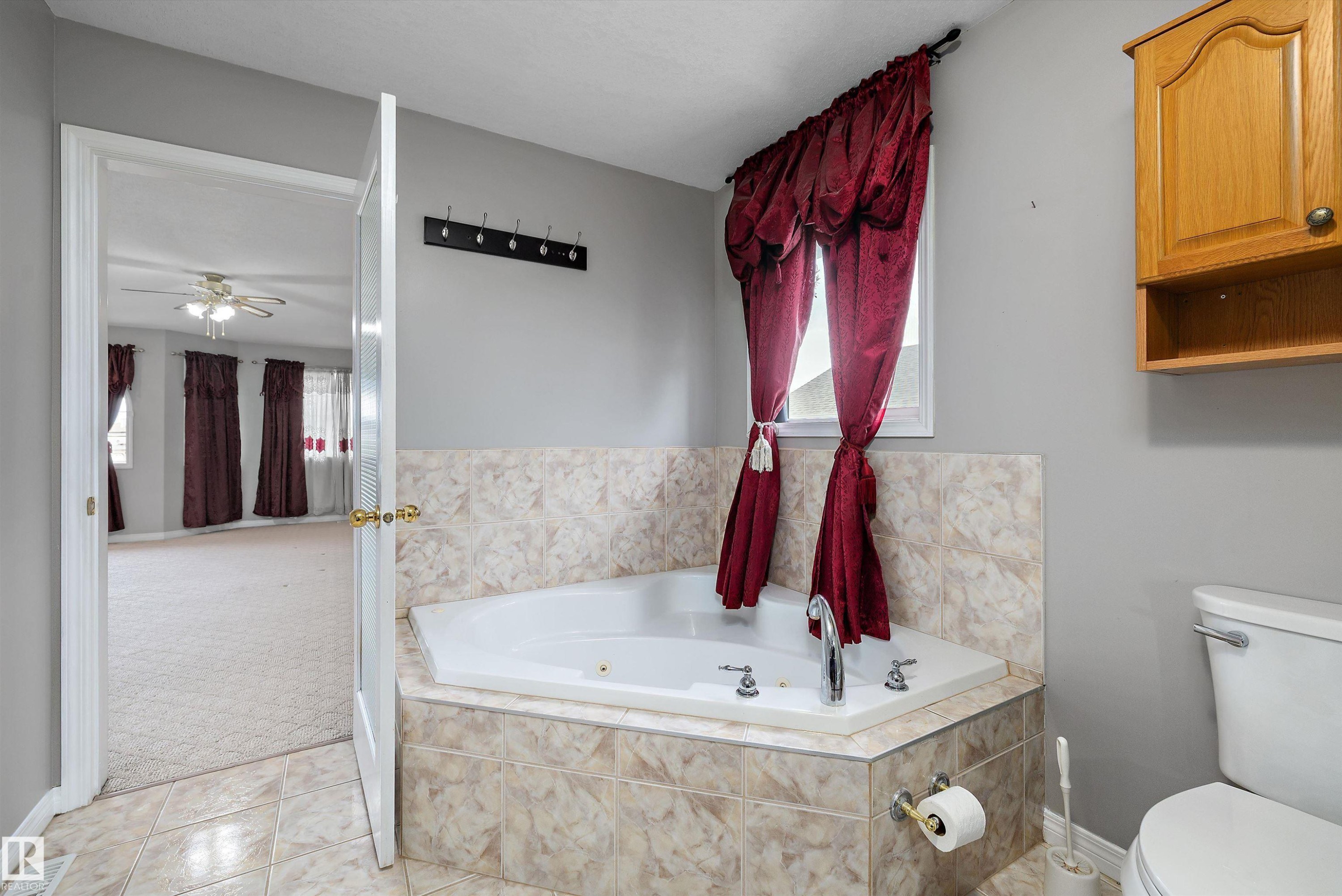 Corner soaking tub with tiled surround, light gray walls, and light-toned tile flooring - 4831 154 Avenue, Edmonton, AB