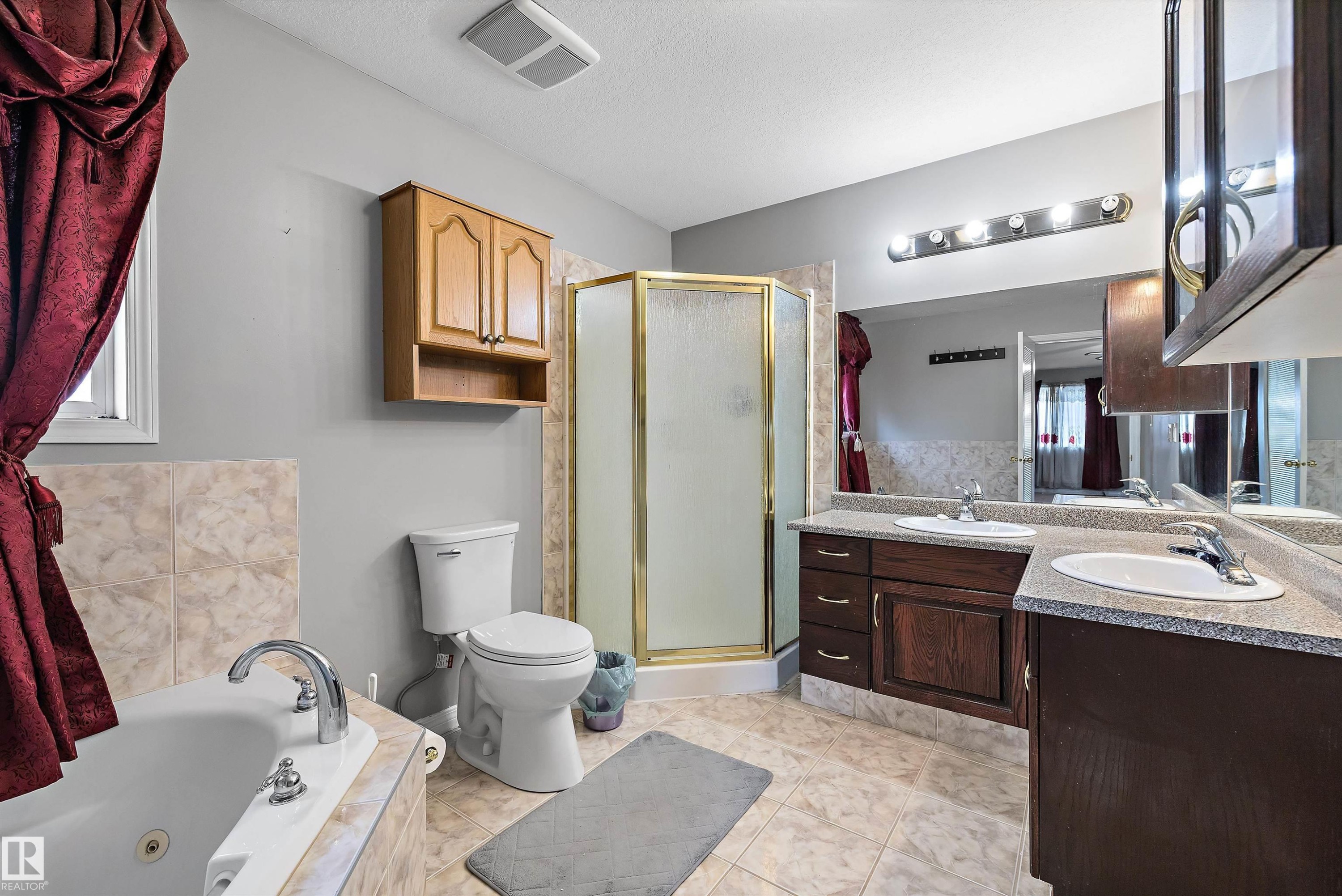 Full bathroom featuring a corner shower with a gold-finish frame, a built-in tub with a tiled surround, a double vanity with integrated sinks and dark wood cabinetry, and a mirrored wall - 4831 154 Avenue, Edmonton, AB
