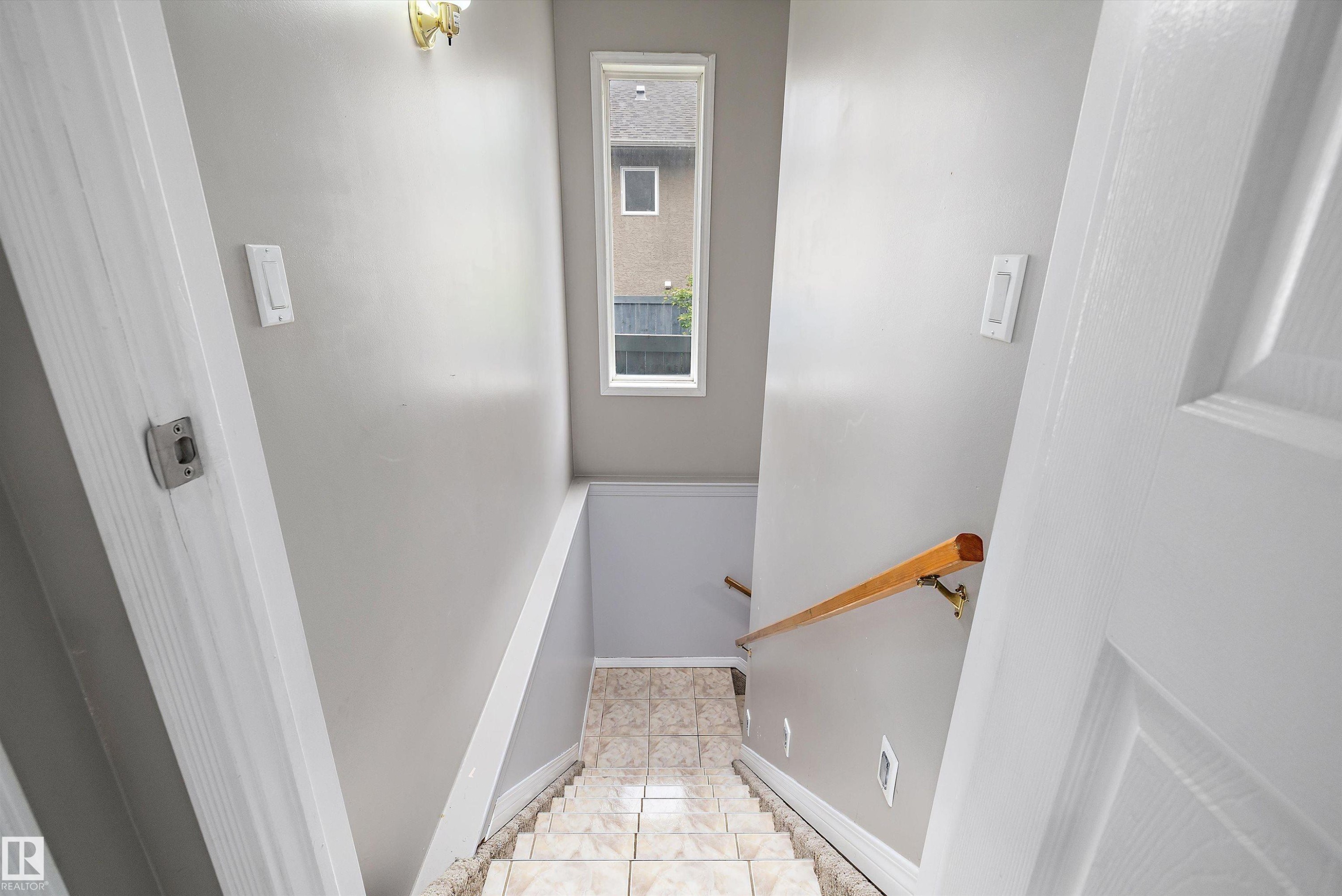 Stairwell featuring tile flooring, light neutral wall paint, and a wood handrail - 4831 154 Avenue, Edmonton, AB
