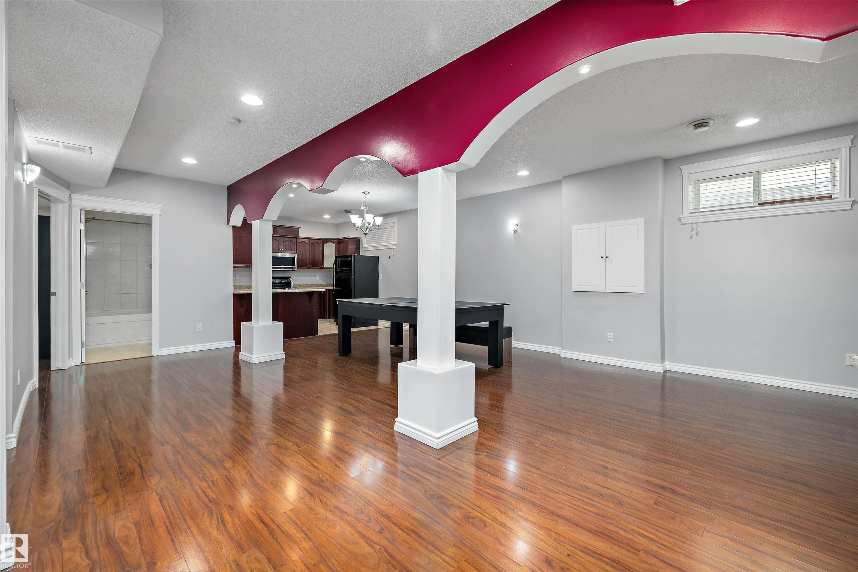 Spacious open-concept area featuring wood-finish flooring, recessed lighting, and decorative archways with accent coloring - 4831 154 Avenue, Edmonton, AB
