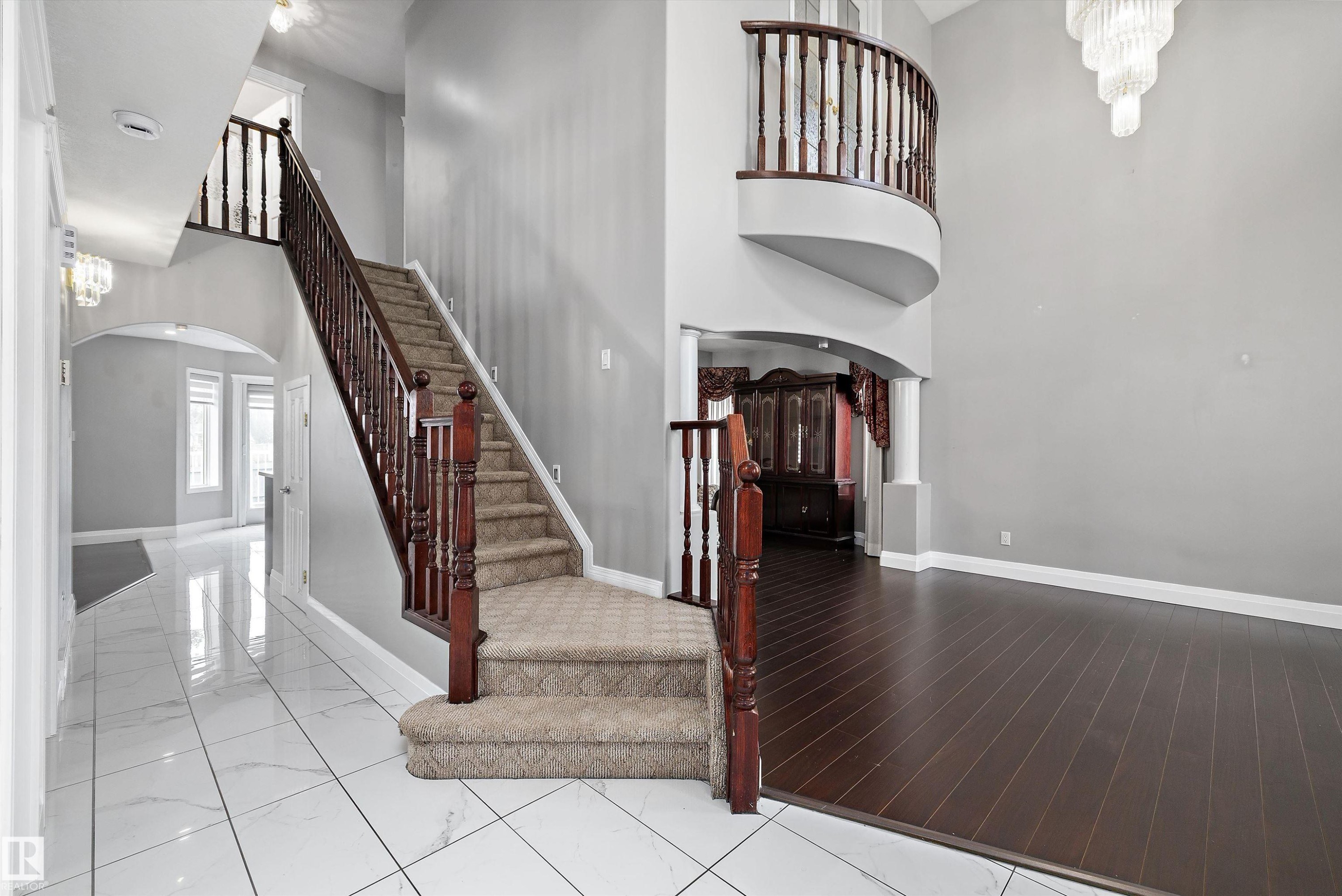 Grand foyer featuring a curved upper balcony, a two-story ceiling, and a prominent staircase with wood railings and carpeted treads - 4831 154 Avenue, Edmonton, AB