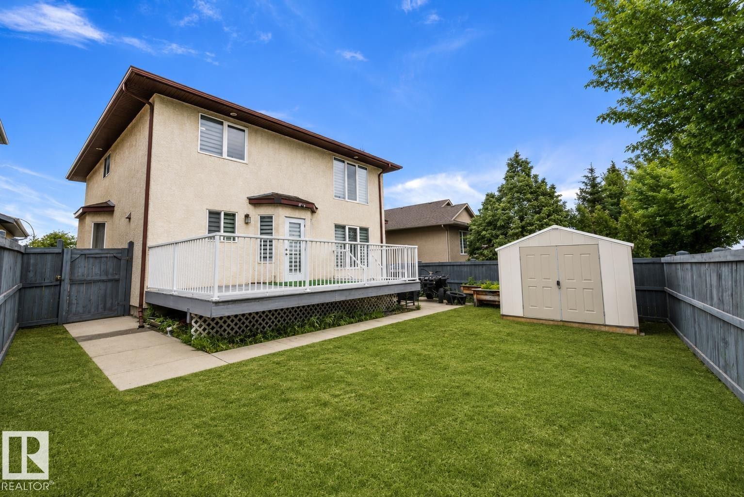 Expansive backyard featuring a manicured lawn, a raised wood-finish deck with white railing, and a detached storage shed - 4831 154 Avenue, Edmonton, AB