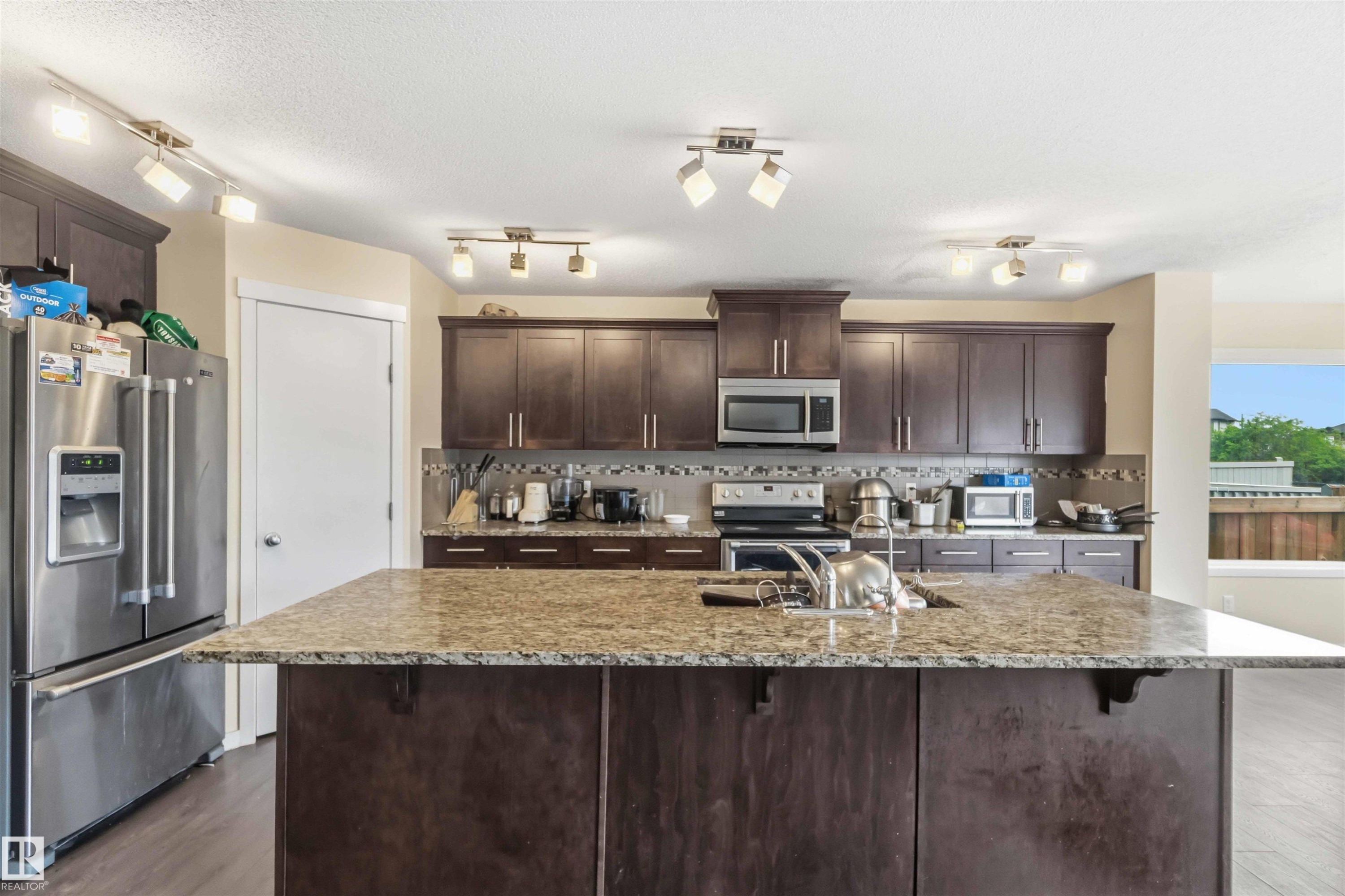 Kitchen island with an undermount sink, granite-style countertop, and dark wood-finish cabinetry - 5120 19 Avenue, Edmonton, AB