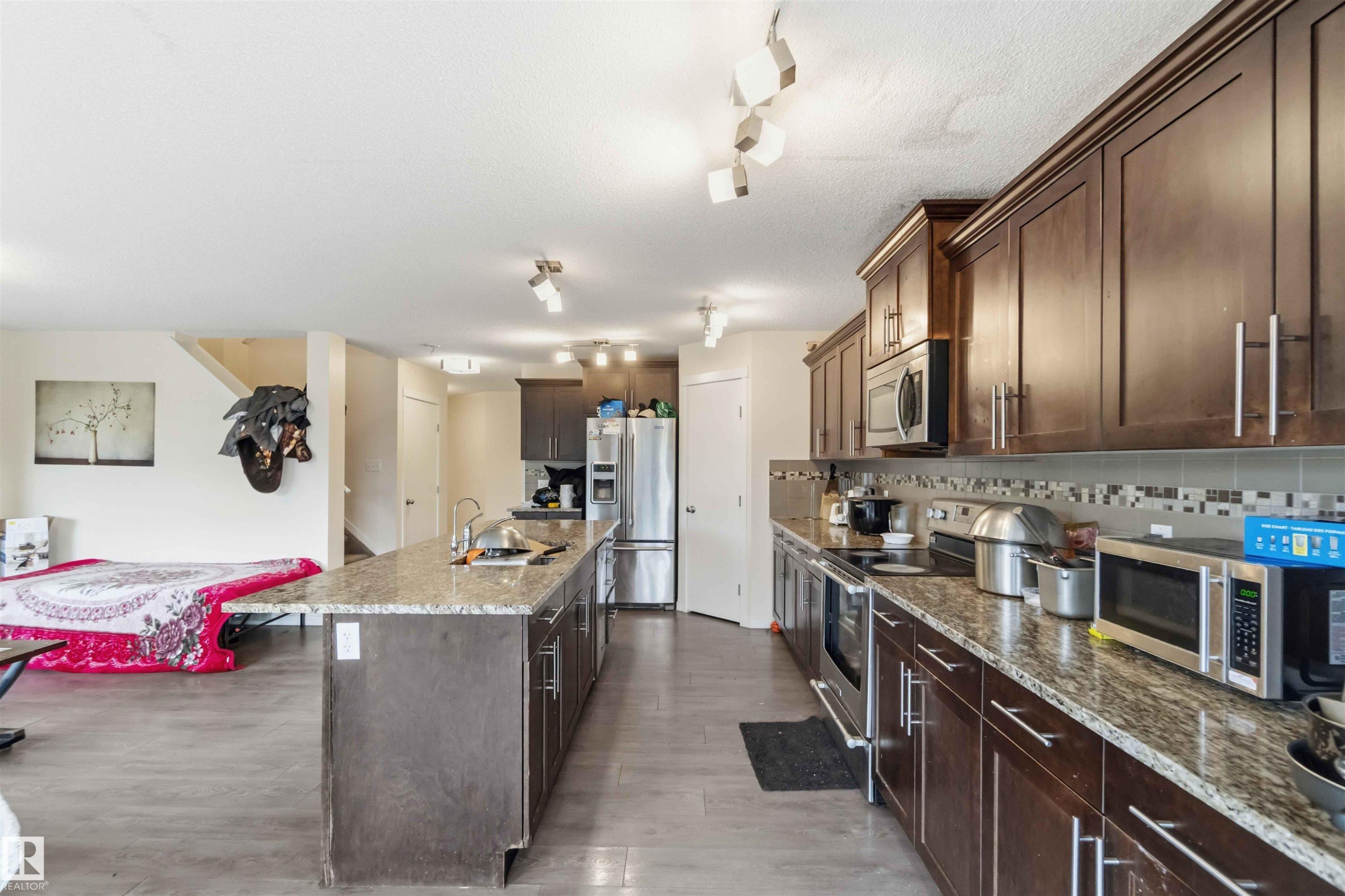 Kitchen featuring wood-finish cabinetry, granite-style countertops, stainless steel appliances, a mosaic tile backsplash, and a large central island with an undermount sink - 5120 19 Avenue, Edmonton, AB
