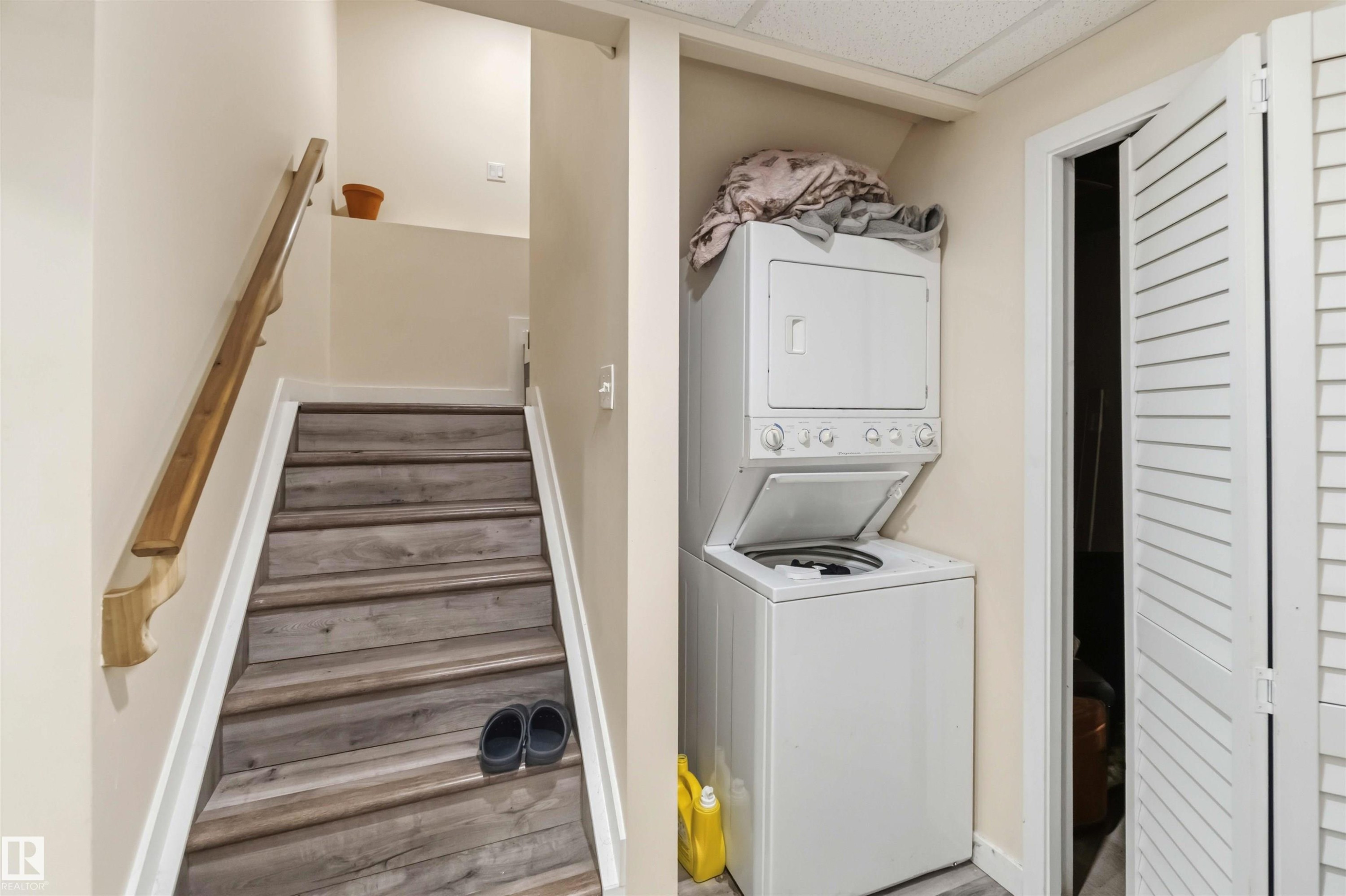 Dedicated laundry area featuring a stacked washer and dryer, adjacent to a staircase with wood-finish treads and a matching handrail - 5120 19 Avenue, Edmonton, AB
