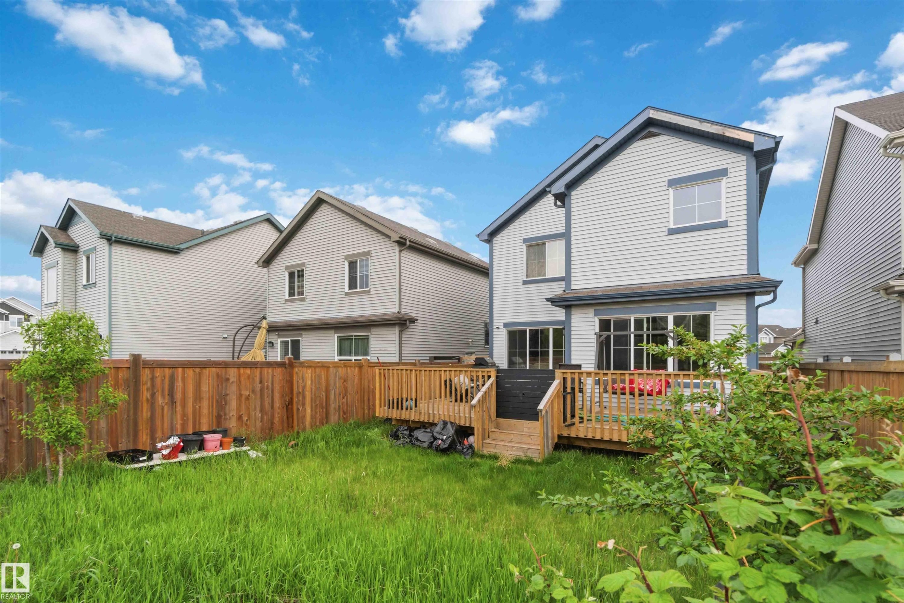 Rear exterior featuring a spacious wood deck, sliding glass doors, white horizontal siding, and a private wood fence - 5120 19 Avenue, Edmonton, AB