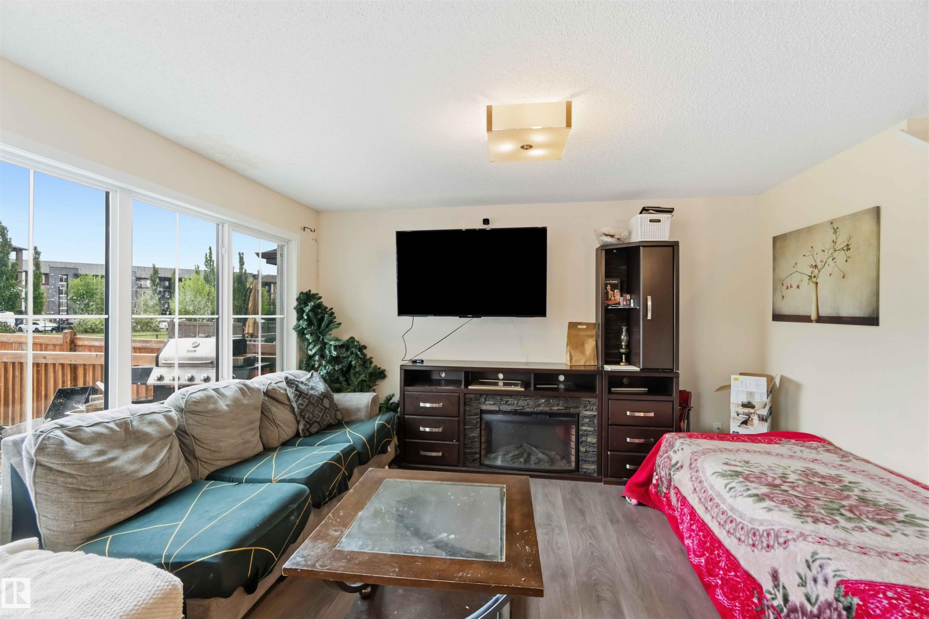 Spacious living area featuring light wood-finish flooring, a built-in electric fireplace with stone-look surround, and ample natural light from extensive sliding glass doors - 5120 19 Avenue, Edmonton, AB