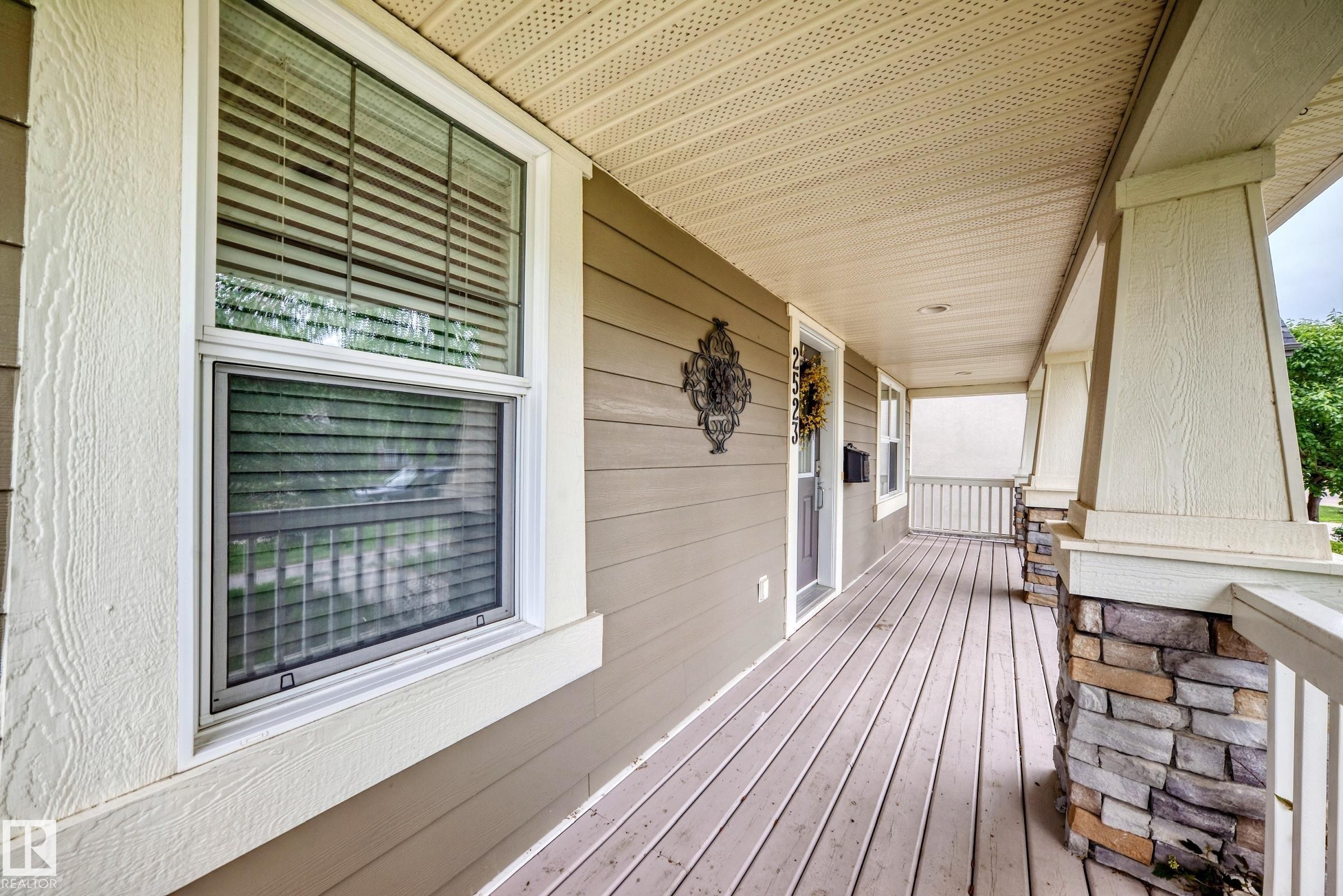 Covered front porch featuring wood-finish flooring, stone-clad pillar bases, and light-toned siding - 2523 Pegasus Boulevard, Edmonton, AB