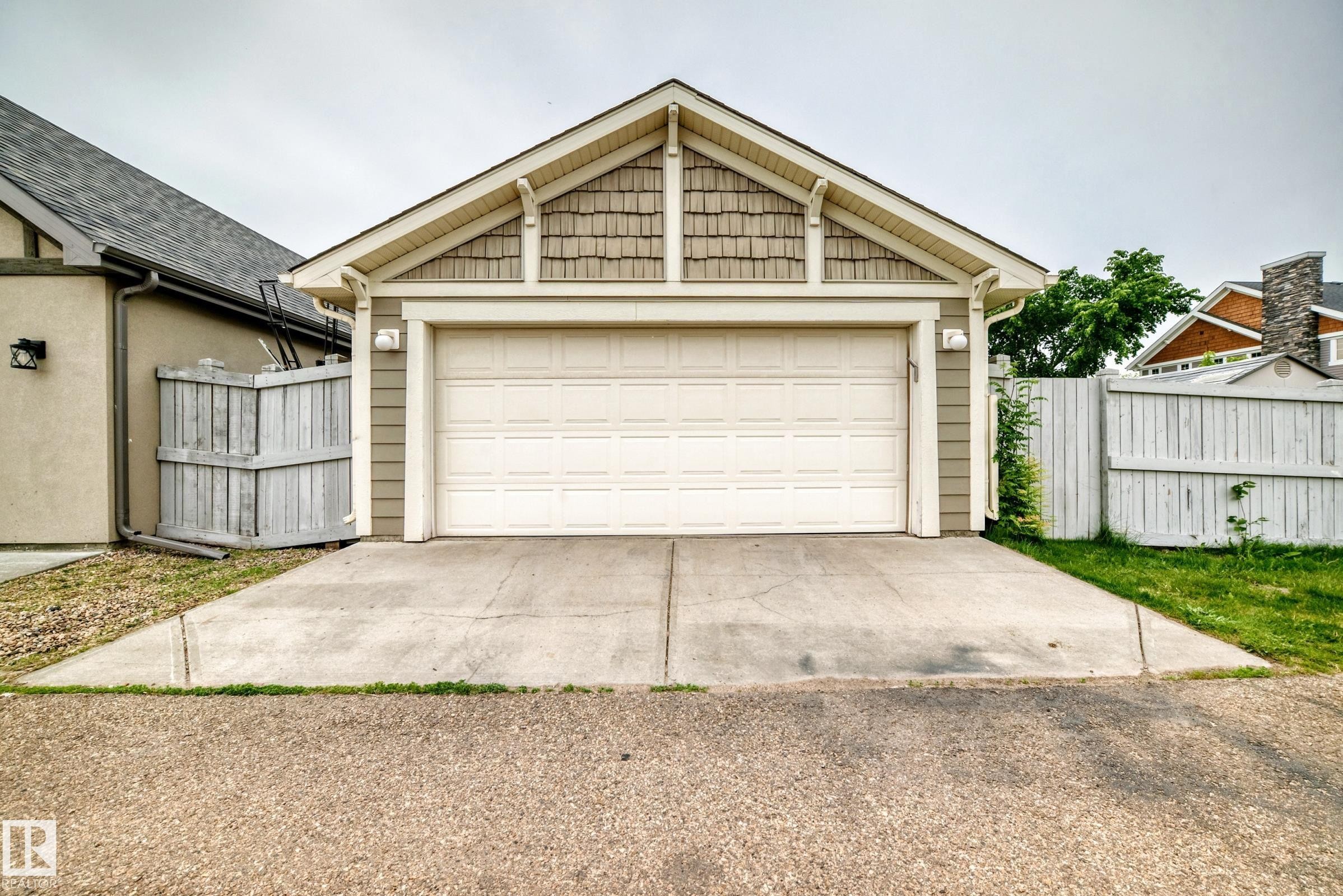 Detached two-car garage with a panel-style garage door, featuring horizontal siding, decorative shingle accents, and an A-frame roof - 2523 Pegasus Boulevard, Edmonton, AB
